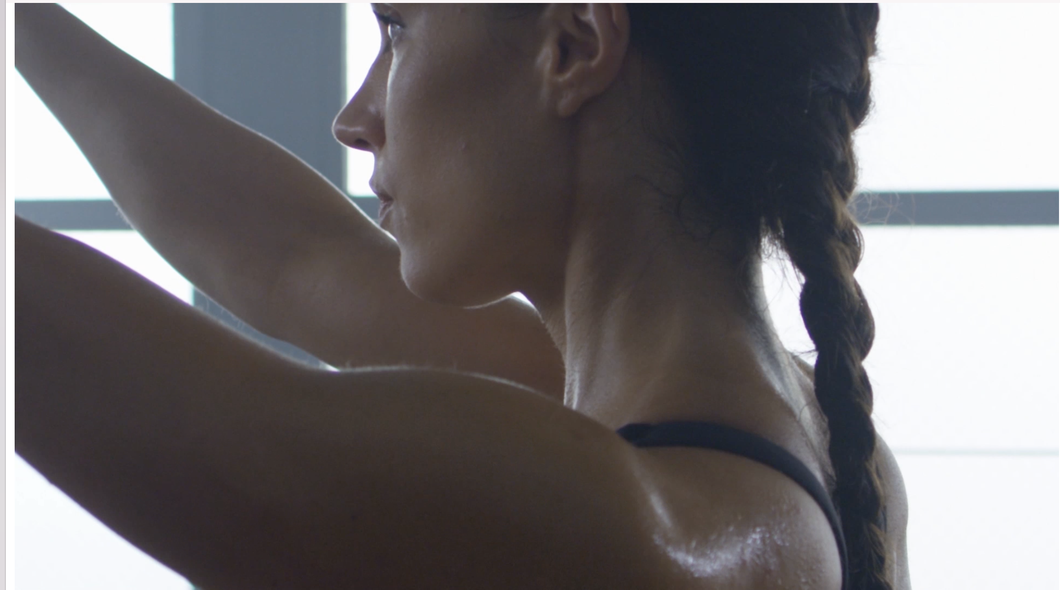 A woman with a braid and sleeveless top stretching against a window.