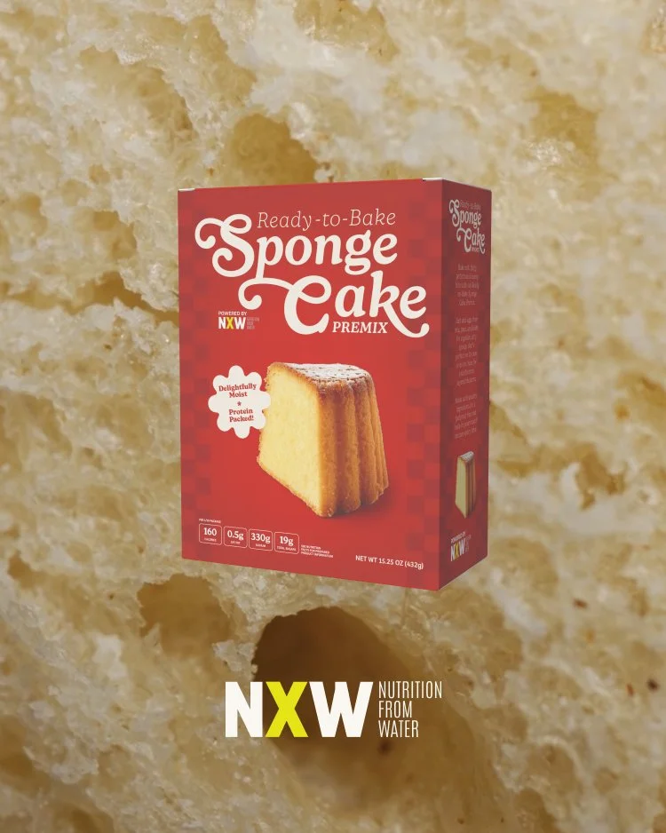 A box of ready-to-bake sponge cake premix with an image of a baked sponge cake on the front, set against a textured background resembling sponge cake interior.