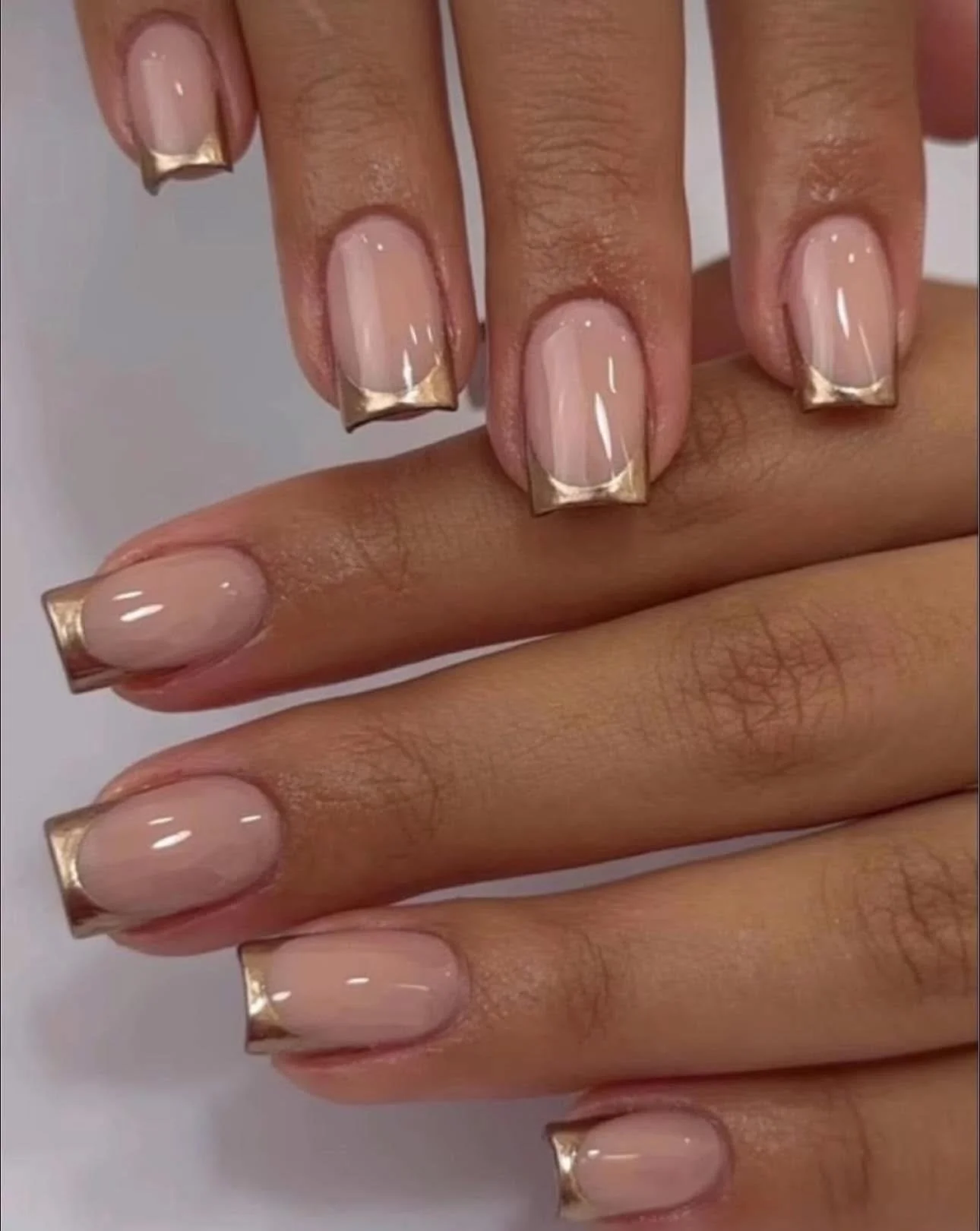 Close-up of hands with manicured nails featuring a French tip design with gold accents.