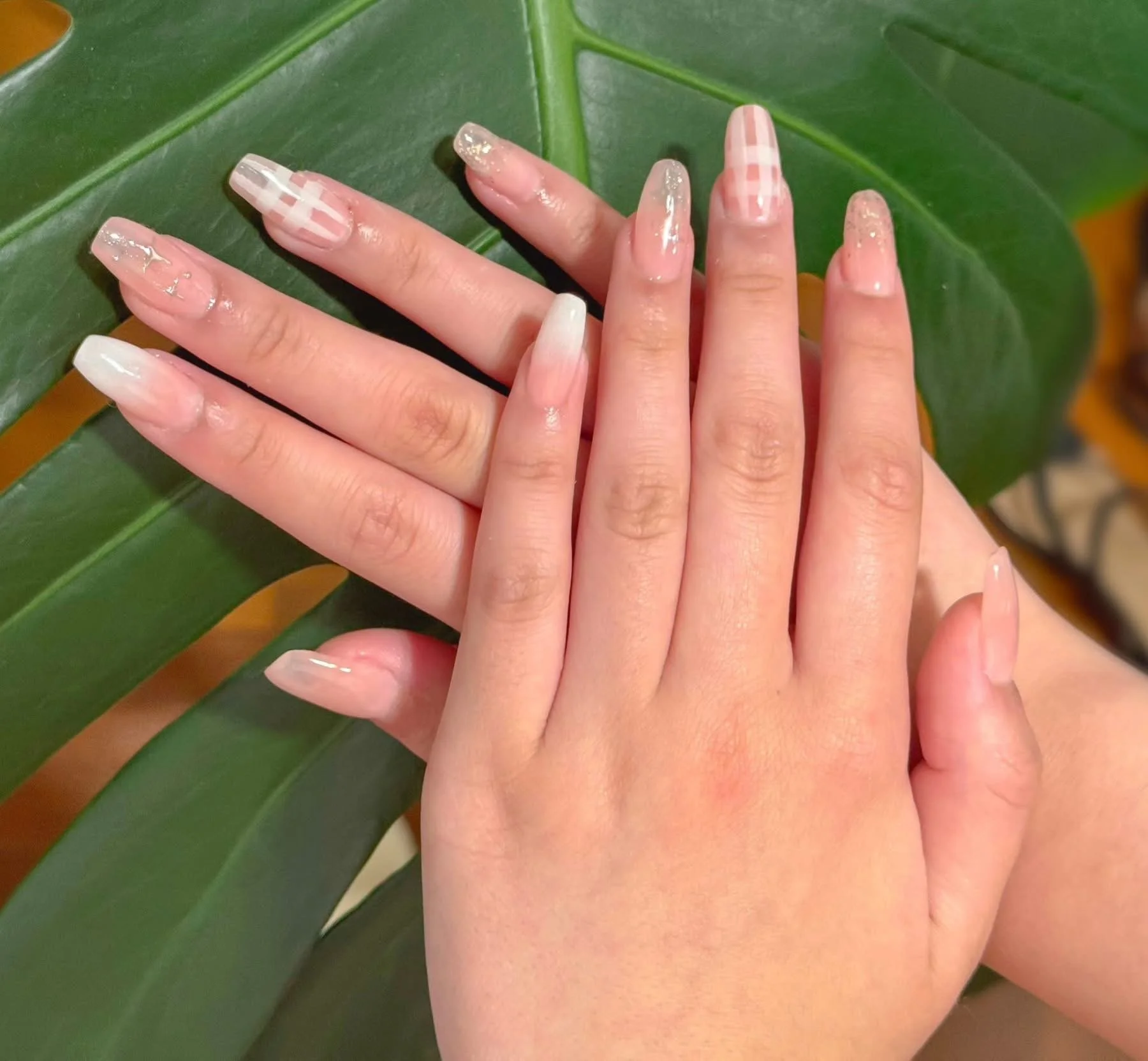 Two hands with manicured nails resting against a large green leaf.