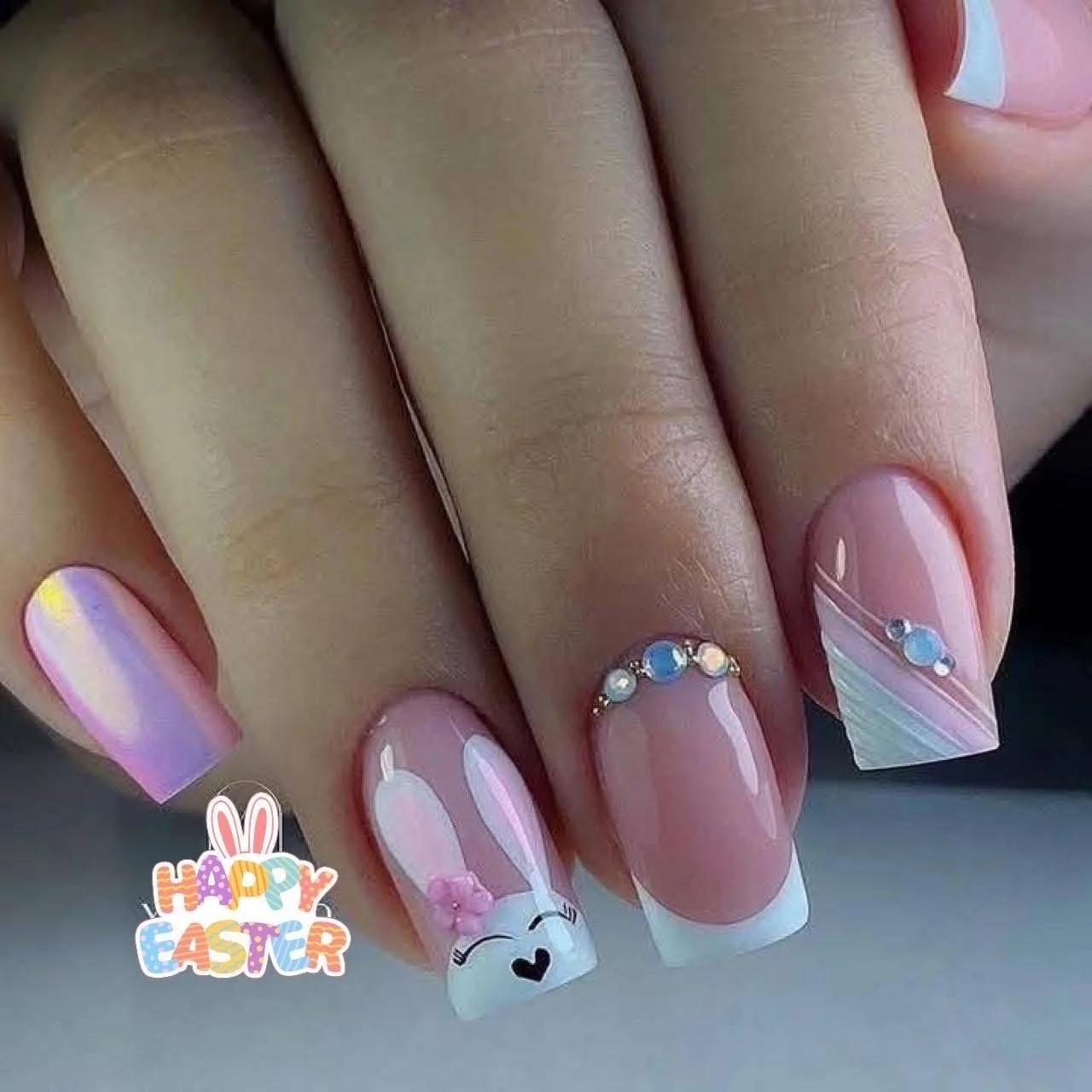 Nail art with pastel colors, floral designs, rhinestones, and an Easter bunny face with a pink bow, along with a "Happy Easter" sticker.