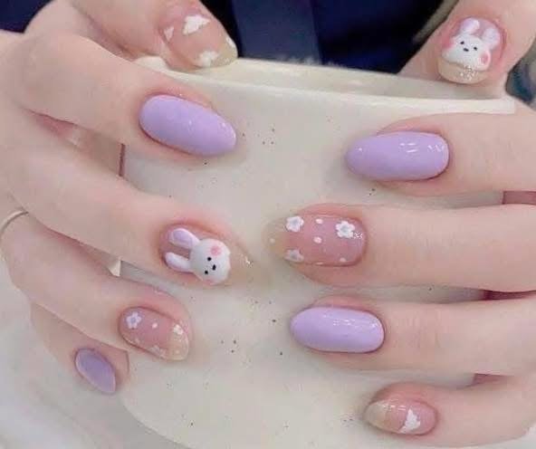 Close-up of a customer's hands with lavender, pink, and decorated nails featuring bunny and snowflake designs.