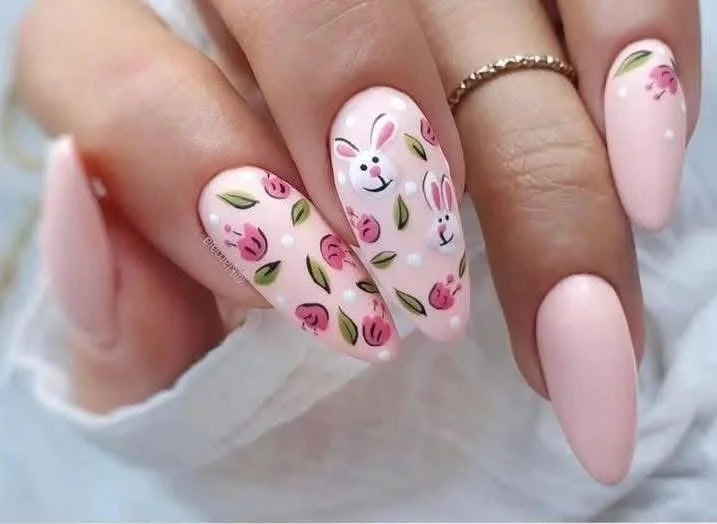 Nail art on a hand with pink nails, featuring a cute bunny face and floral patterns with pink flowers and green leaves.