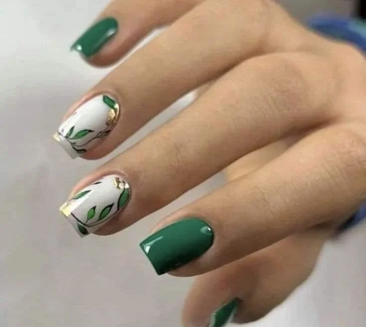 Close-up of a hand showing manicured nails with green polish and a floral design on some nails.