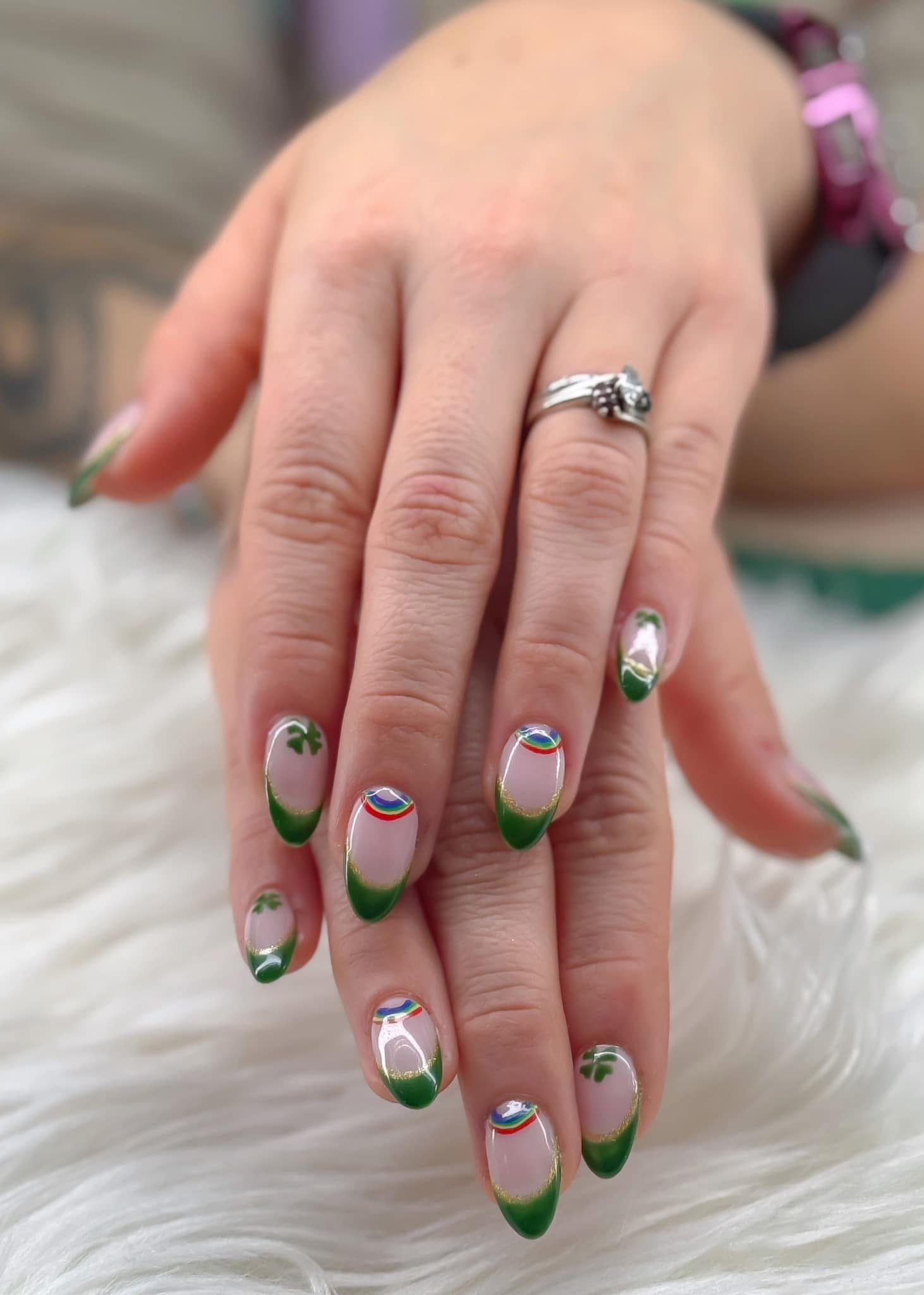 Close-up of a customer's hands with colorful rainbow and green clover nail art, wearing a silver ring with a gemstone, resting on a white fluffy surface.