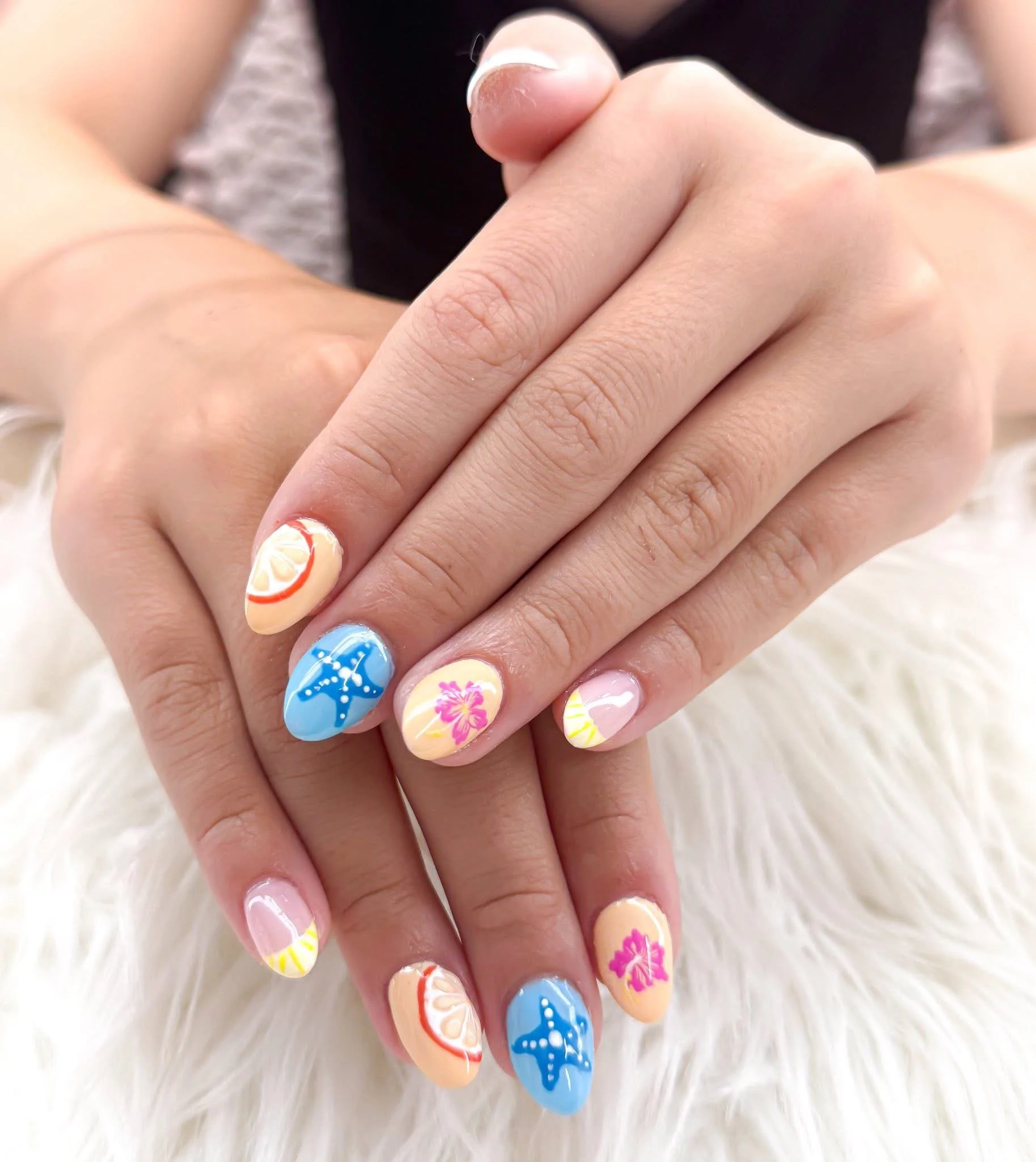 Colorful beach-themed nail art with lemon slices, starfish, and hibiscus flower designs on fingernails.