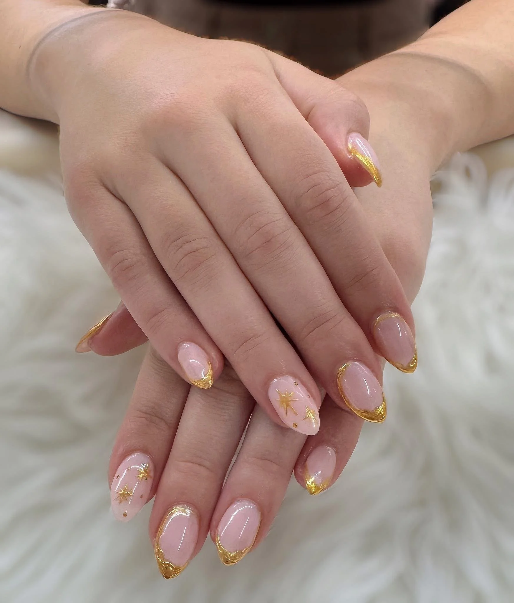 Hand with manicure featuring clear nails with gold tips and small star designs.