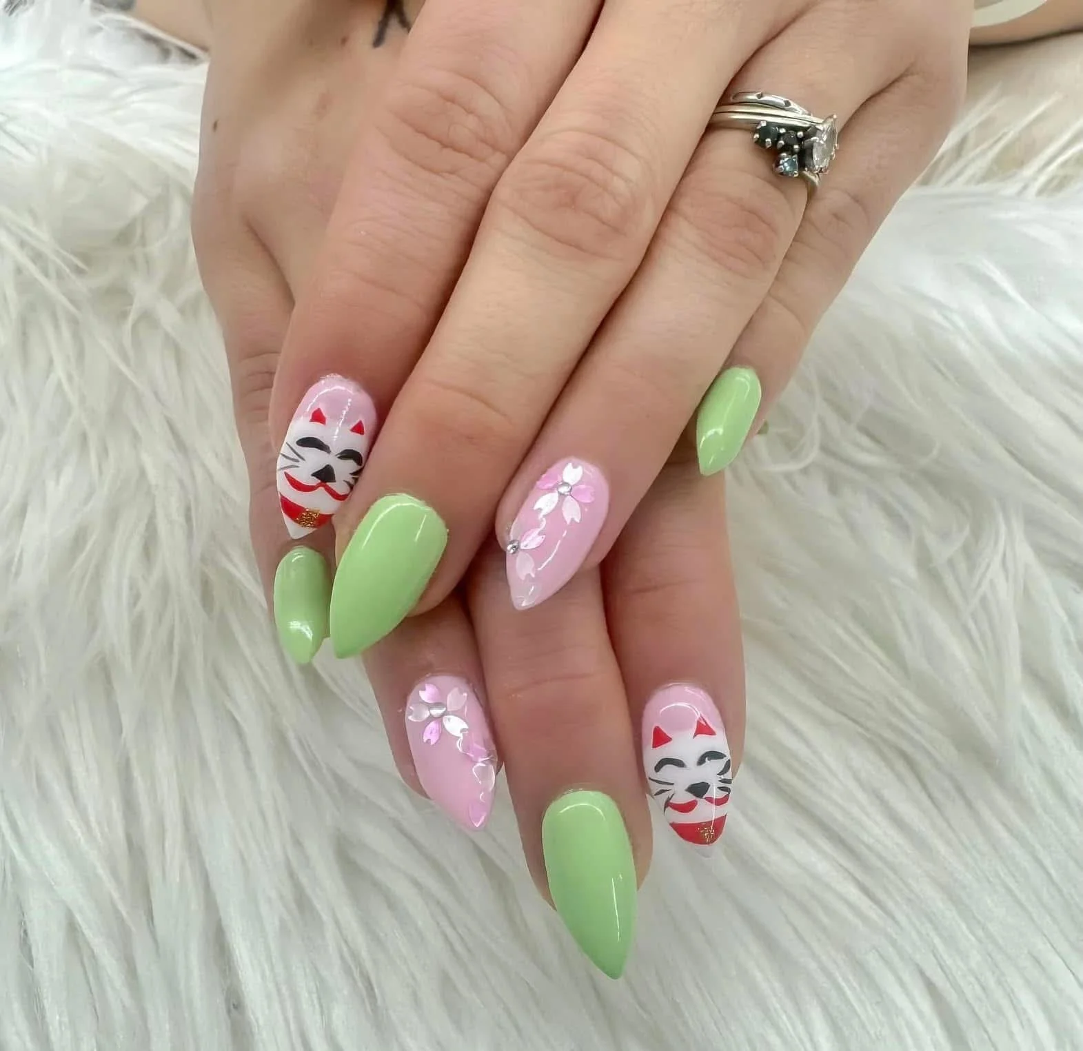 Manicure with lime green nails, pink nails with white flowers, and nails with a Japanese lucky cat design.