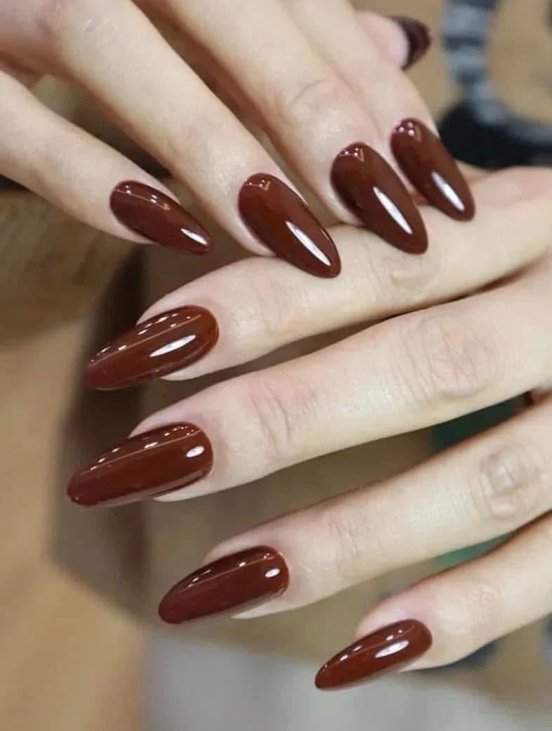 Close-up of a hand with long, almond-shaped nails painted in glossy dark red or burgundy polish.