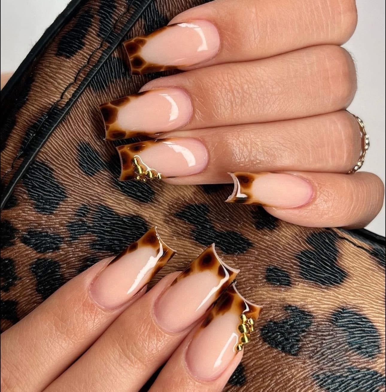 Close-up of a customer's hand with manicured nails featuring leopard print design on the tips, holding a piece of leopard print fabric.