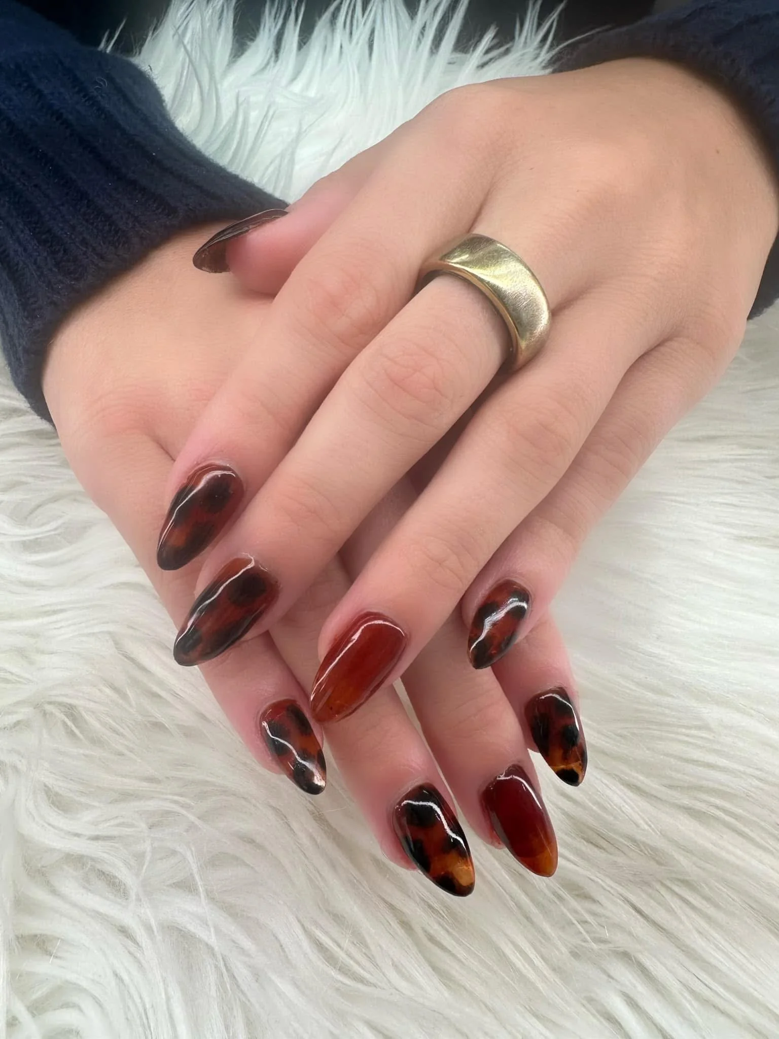 Close-up of a customer's hands with tortoiseshell patterned nail polish, wearing a gold ring on the middle finger, resting on a white furry surface.