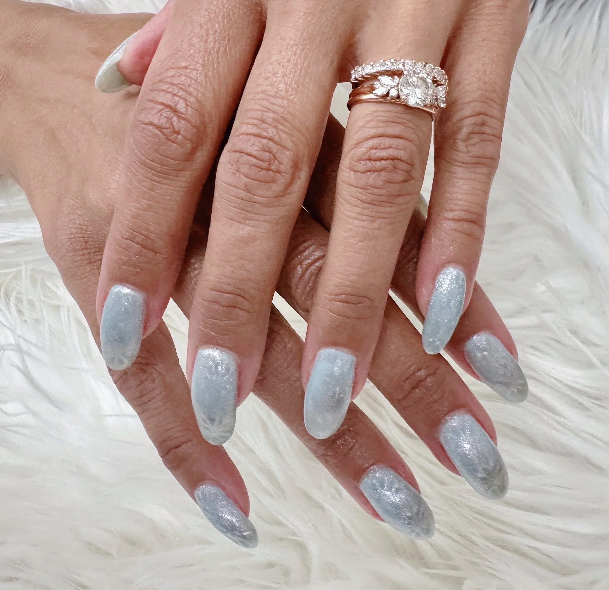 Close-up of a customer's hands with silver glitter nail polish, showing a gold ring with diamonds on her ring finger, resting on a white furry surface.