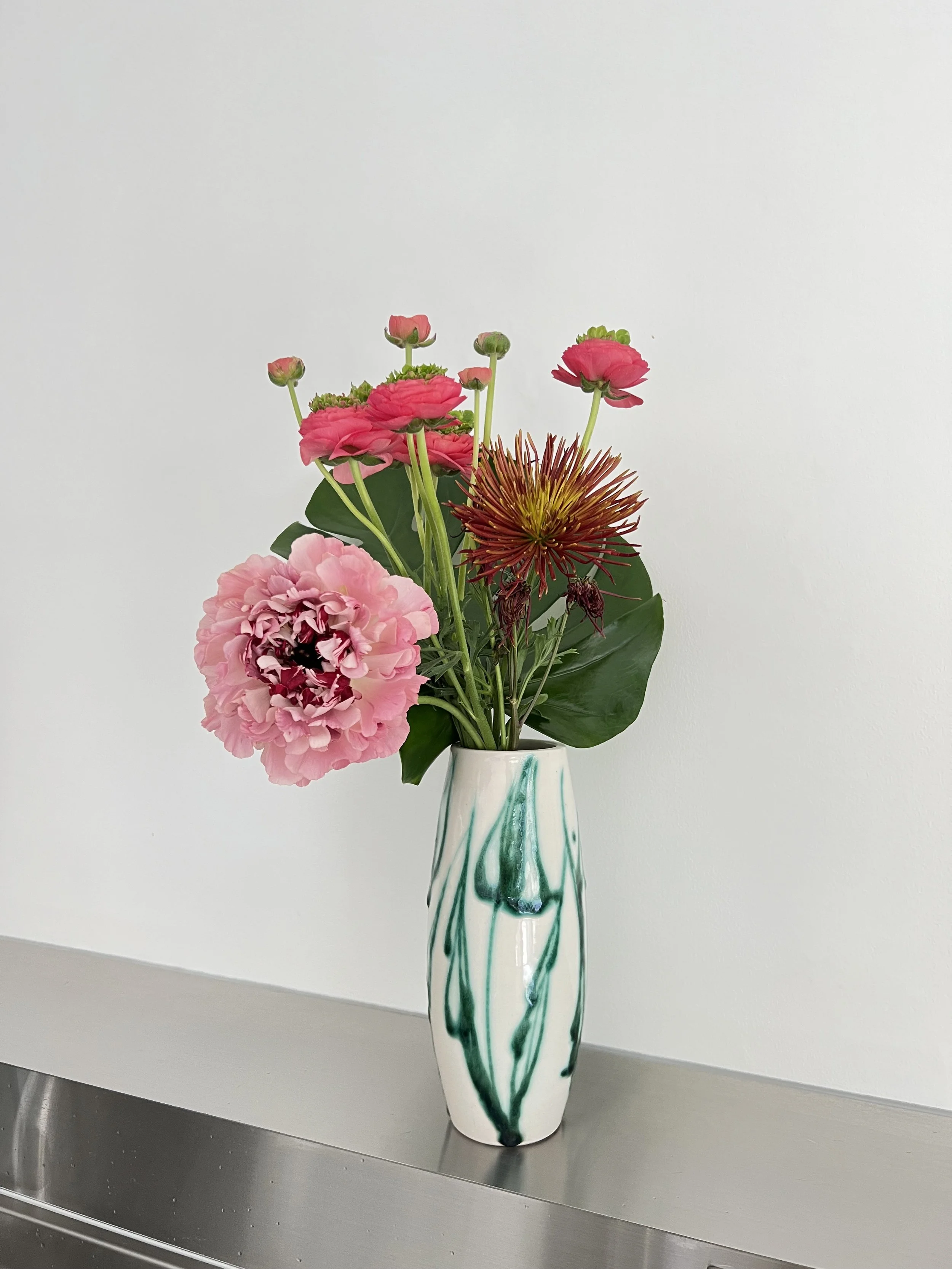 ピンクの花と個性的な花器を合わせた室内のフラワーアレンジメント。Indoor floral arrangement with pink blossoms in a sculptural ceramic vase.