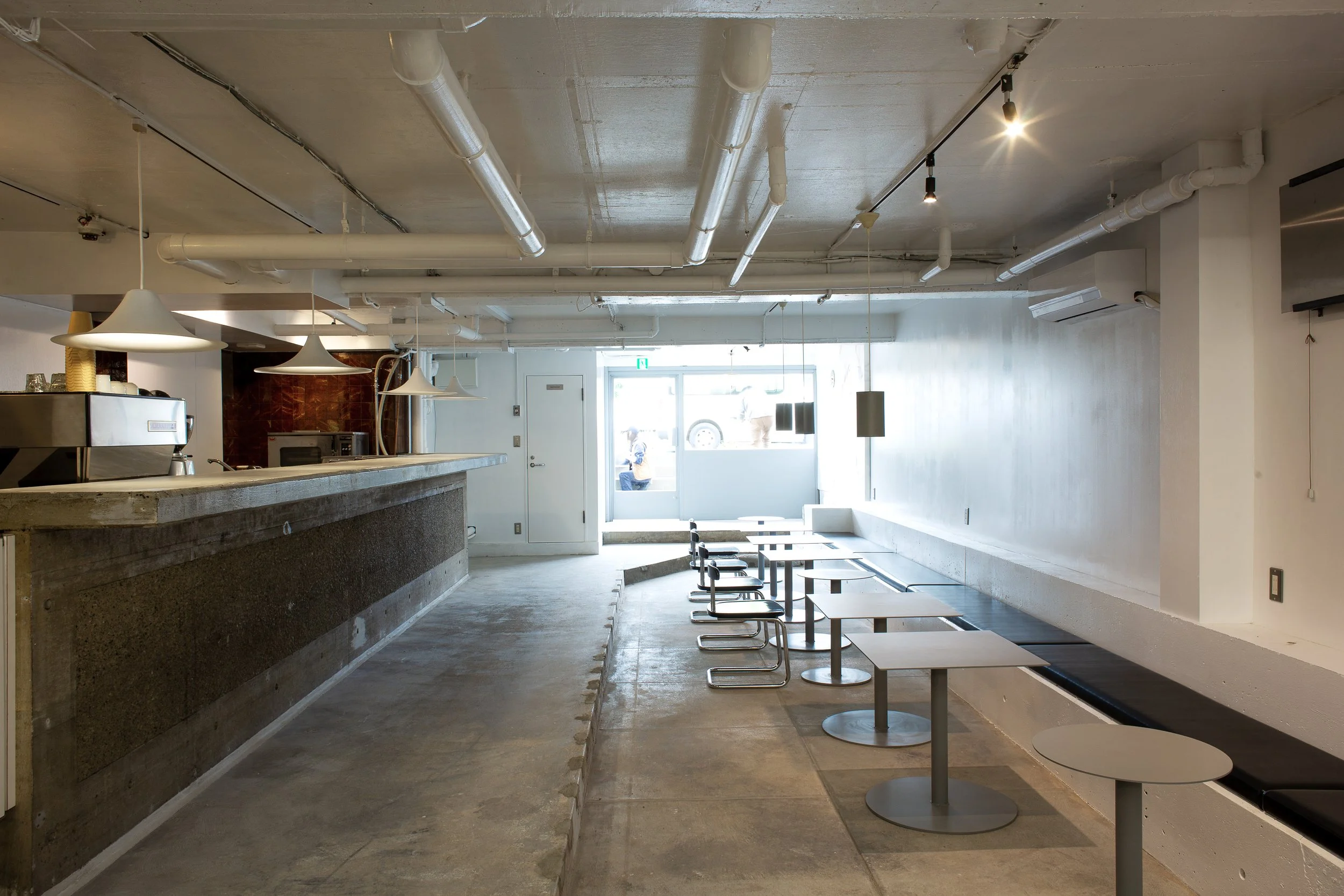 札幌のカフェTRAIL HUTの店内全景。コンクリートカウンター、ロングベンチ、ミニマルな家具で構成された空間をサトウアサミがディレクション。