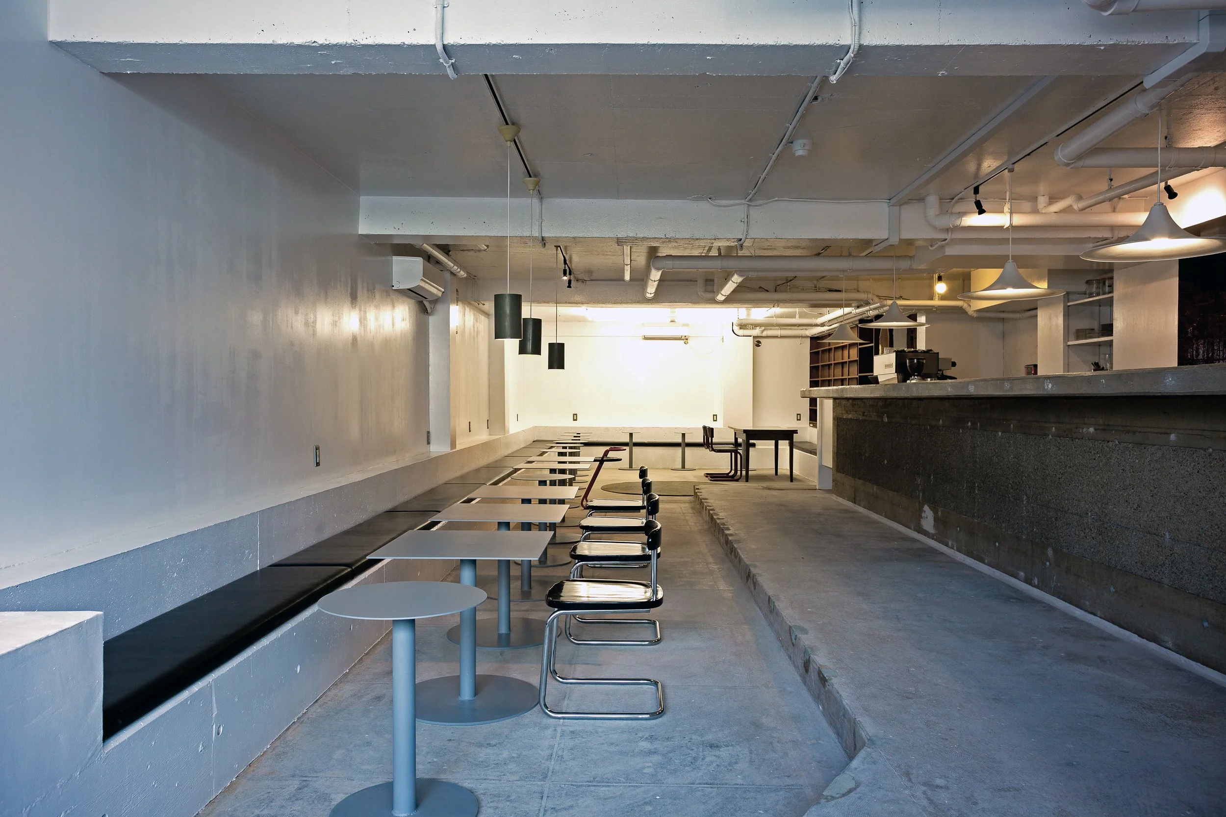TRAIL HUTの店内全景。コンクリート床、ロングベンチ、小さなテーブルが並ぶミニマルで静かなカフェ空間。