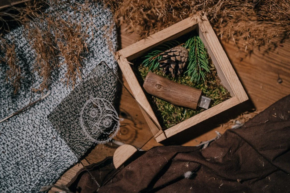 View of a wooden box decorated with pinecones, pine branches, and moss, with a small wooden flashlight, on a wooden floor among Christmas decorations and garlands.