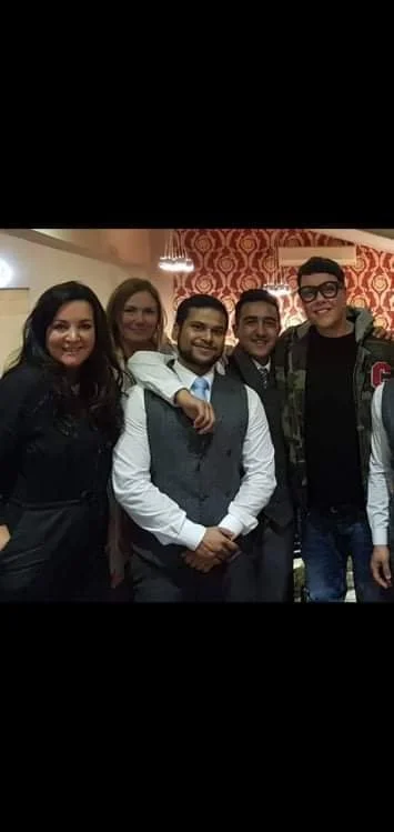 Five people posing together indoors in a warmly decorated room.