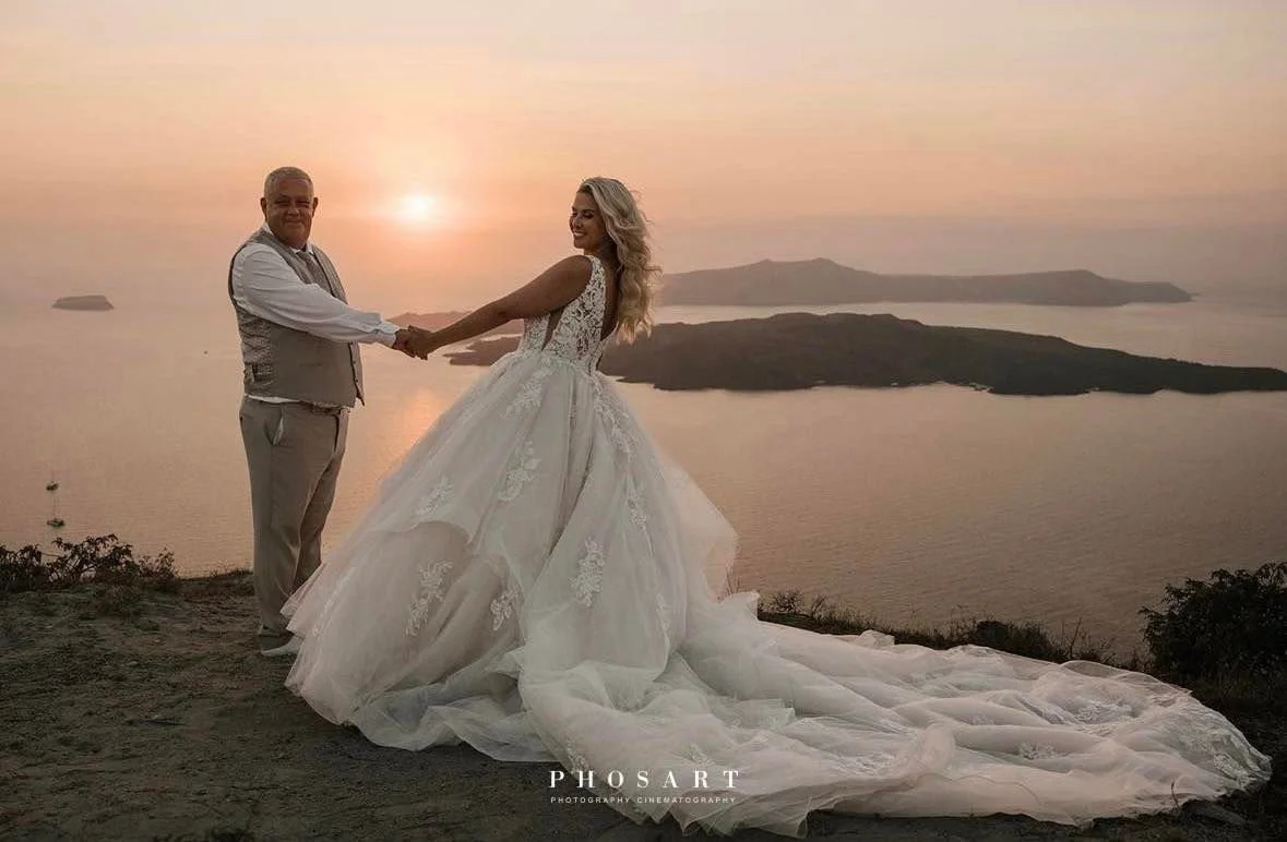 A bride and groom holding hands and smiling at each other during sunset, with a scenic view of water and islands behind them.