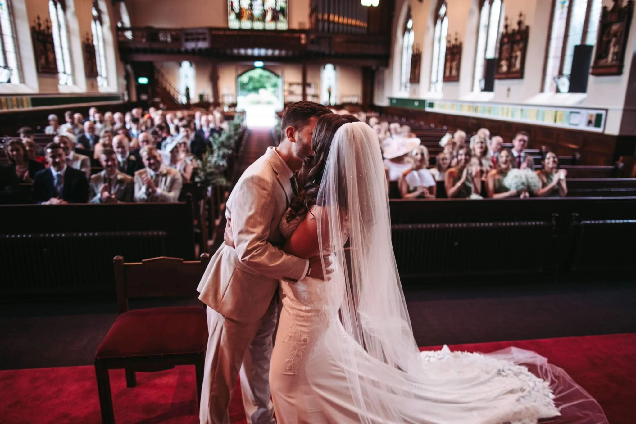 A bride and groom sharing a kiss during their wedding ceremony inside a church, with guests seated in the background.