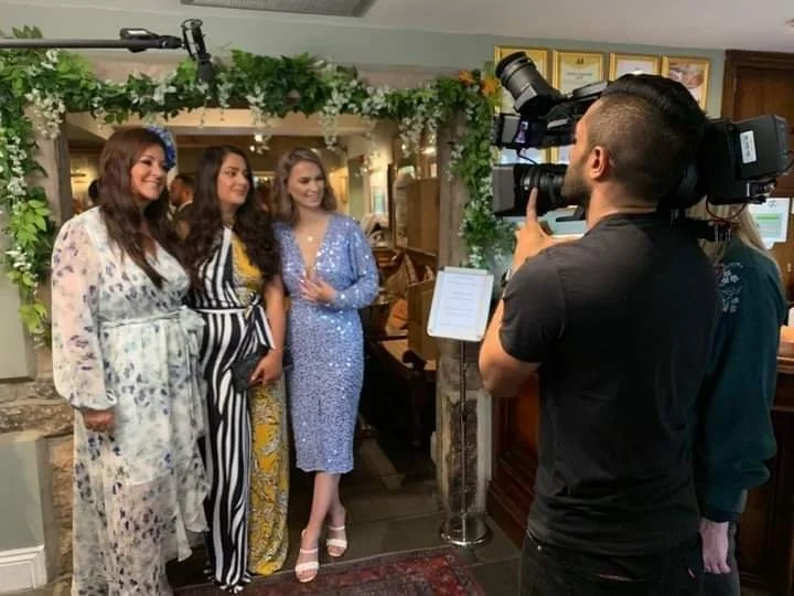 Four women being interviewed or photographed with a professional camera inside a decorated indoor space.