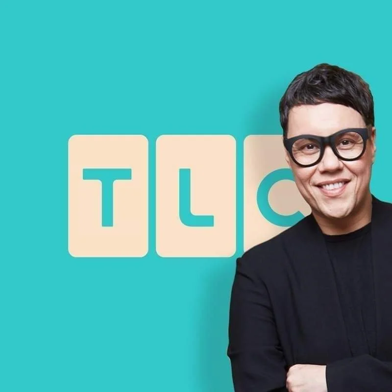 Television host in black glasses and blazer smiling with folded arms in front of a teal background with the TV show logo 'TLC'.