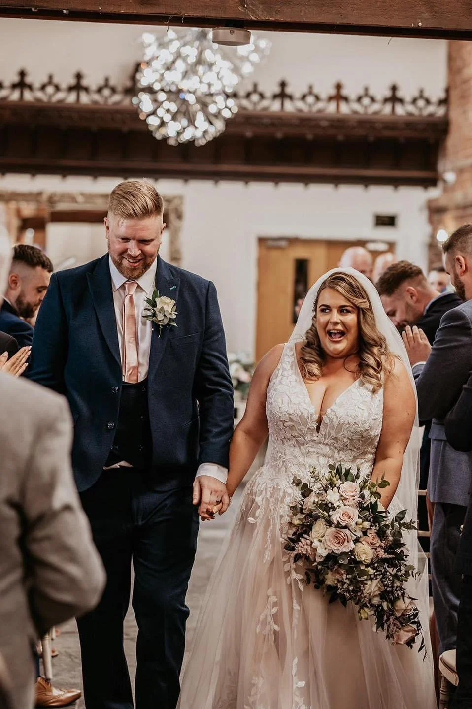 A bride and groom holding hands and walking down the aisle at a wedding ceremony inside a church, with guests in the background.