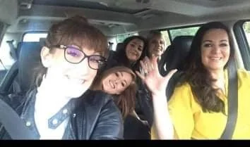 Four women sitting inside a car, smiling and posing for a selfie.