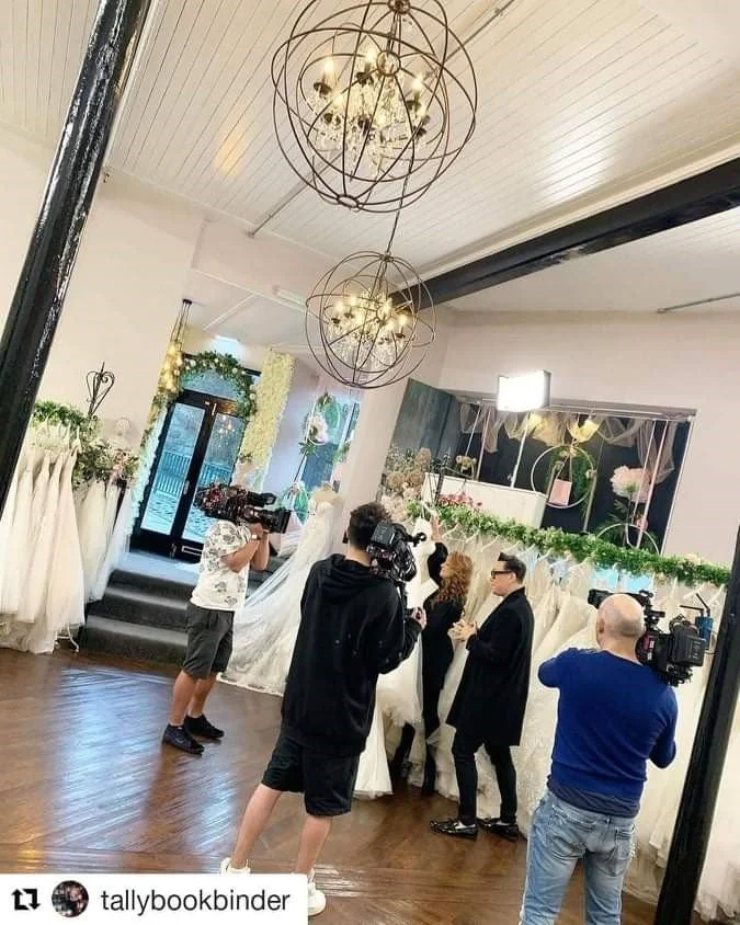 People filming a couple at a wedding ceremony indoors decorated with flowers and drapery.