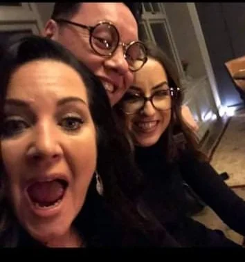 Three women smiling and taking a selfie together indoors.