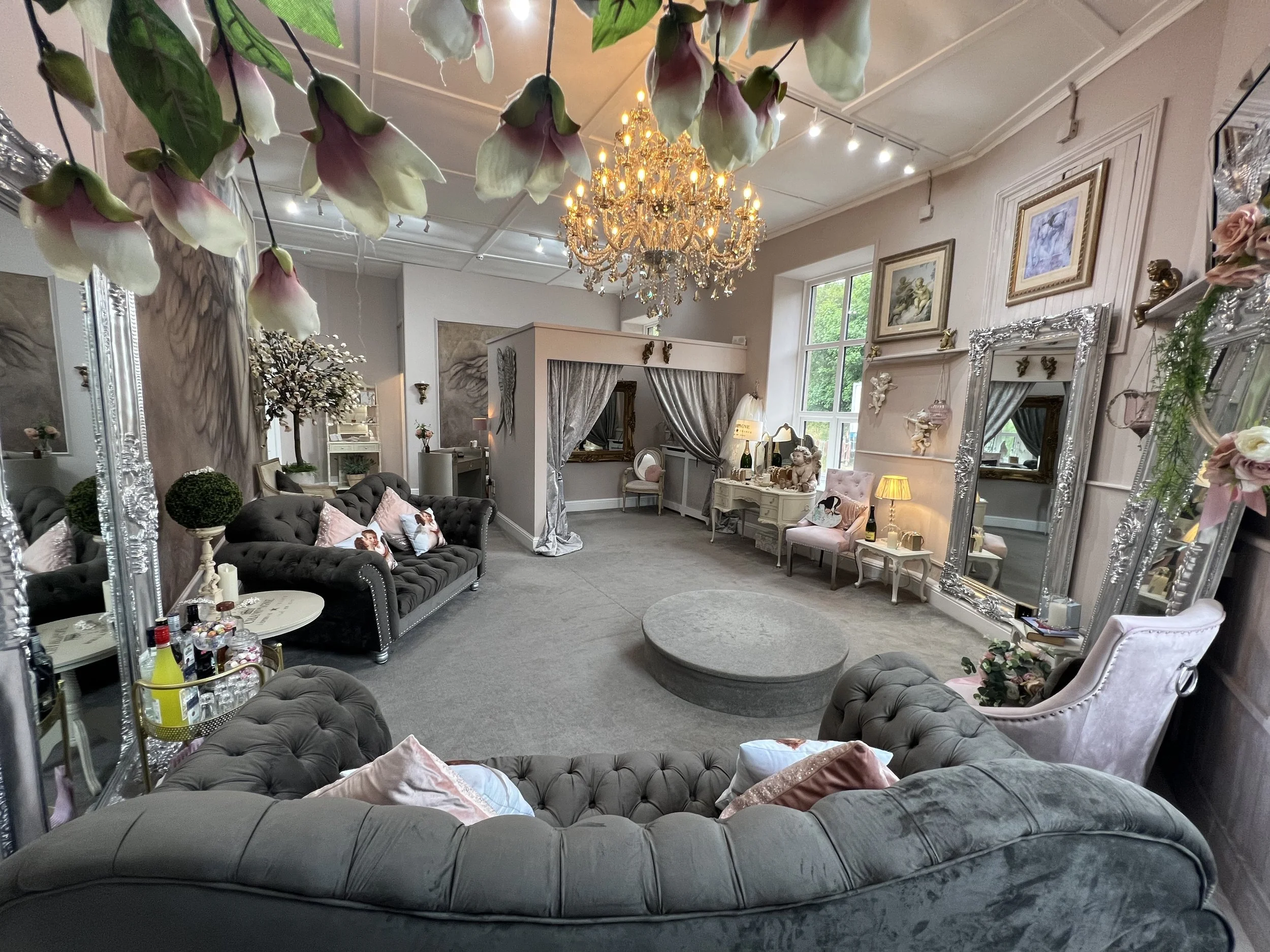Elegant vintage living room with chandelier, large mirrors, velvet sofas, floral decorations, and soft lighting.
