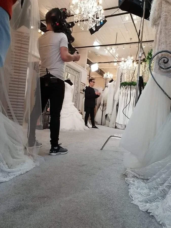 Filming of a wedding dress advertisement in a bridal boutique with crew members documenting the process.