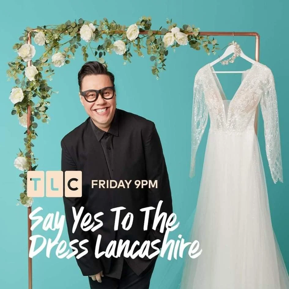A smiling man in black clothing and glasses standing next to a wedding dress hanging on a copper clothing rack. The background is teal, with a floral decoration of white roses and greenery on the top left corner. The image promotes a TLC show called