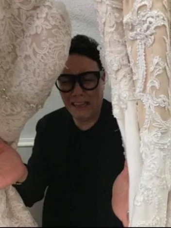 A person with glasses and a black shirt is visibly upset, surrounded closely by intricately designed white lace fabric.