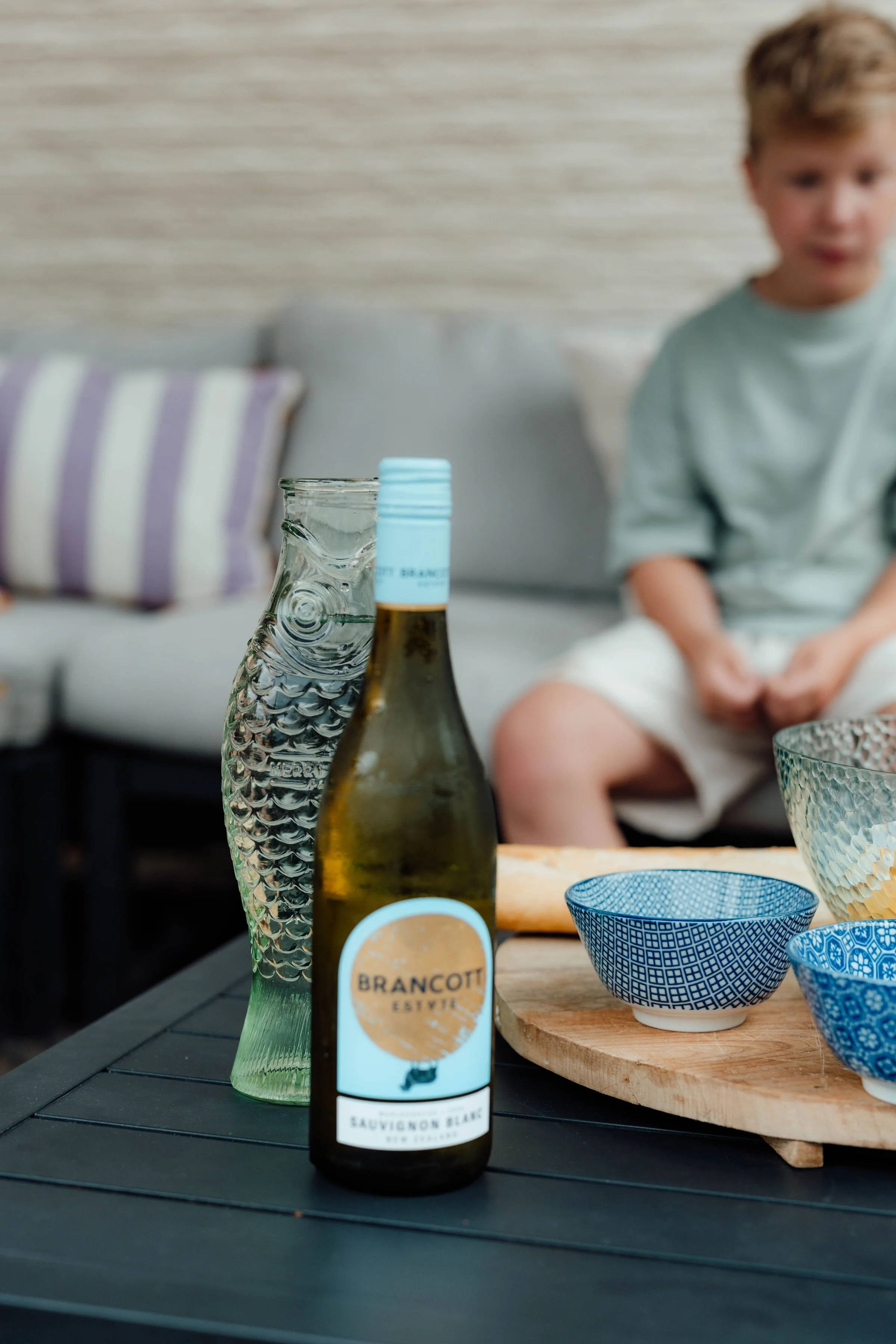 Een fles witte wijn binnen het samengestelde gezin en een visvormige vaas op een tafel, met een jongen op de achtergrond.