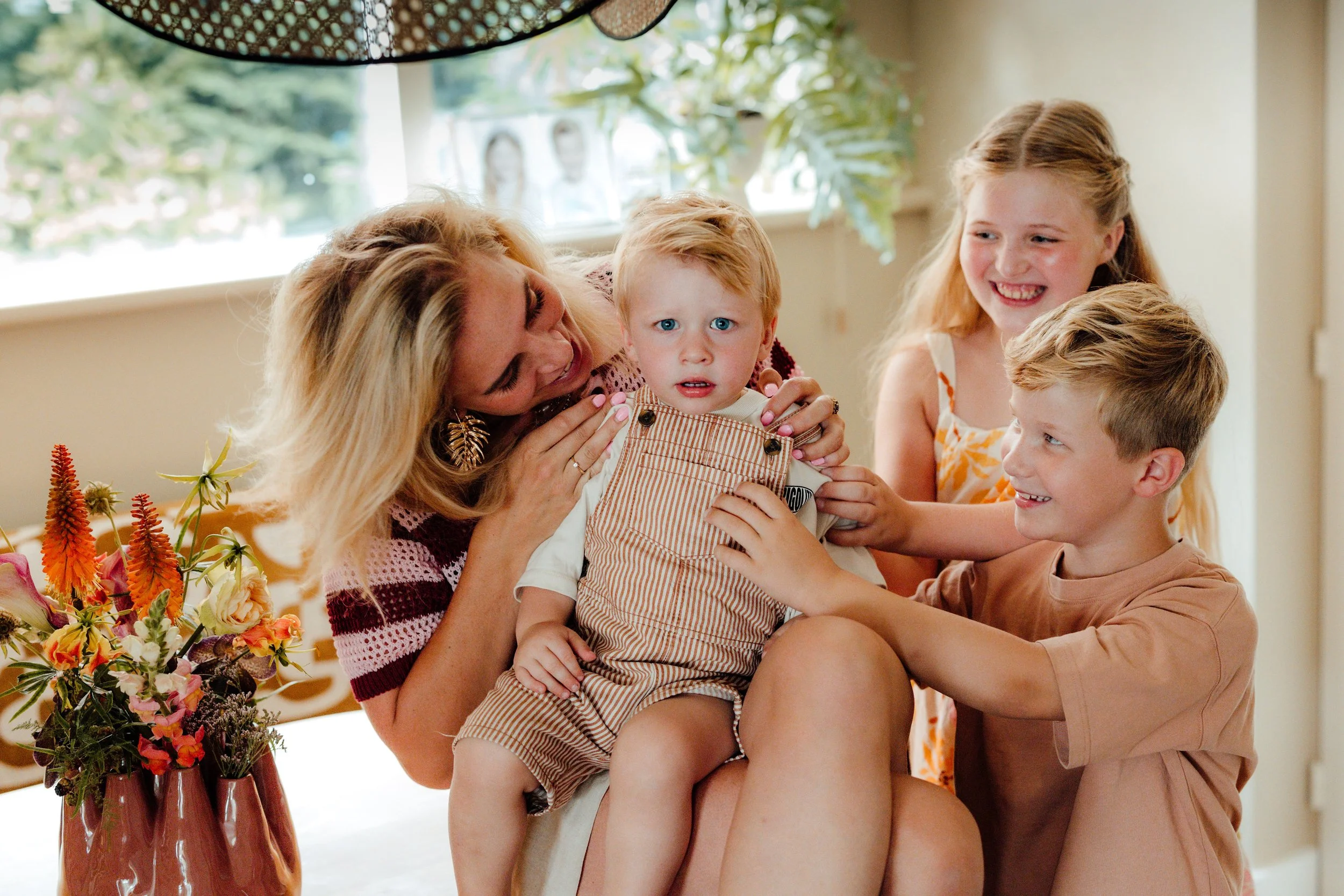 Een bonusmoeder en drie kinderen lachen en spelen samen, terwijl de baby in haar schoot zit.