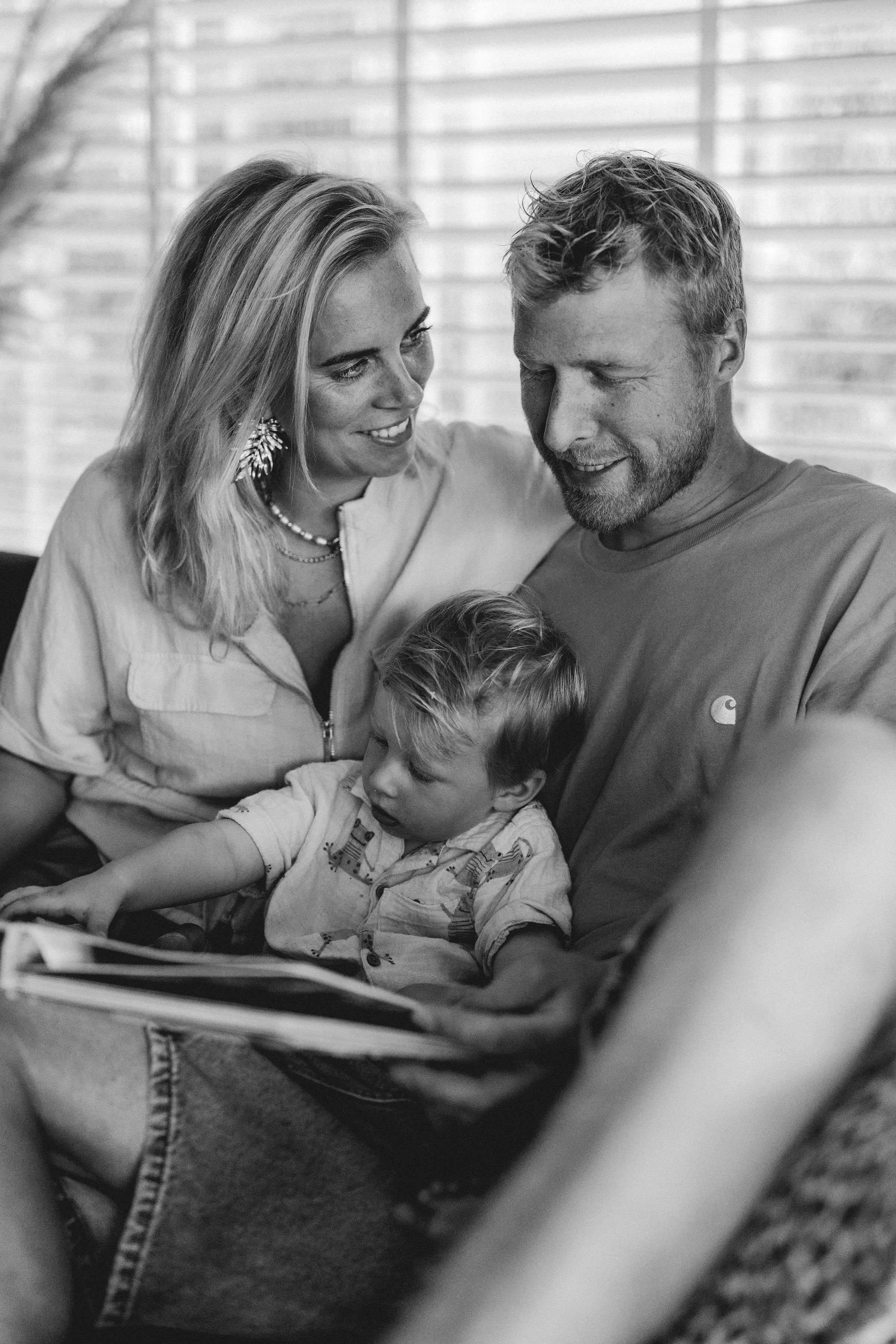 Samengesteld gezin bestaat uit een bonusmoeder, een vader en hun zoon, die samen lezen en elkaars gezichten glimlachend bekijken, binnen.