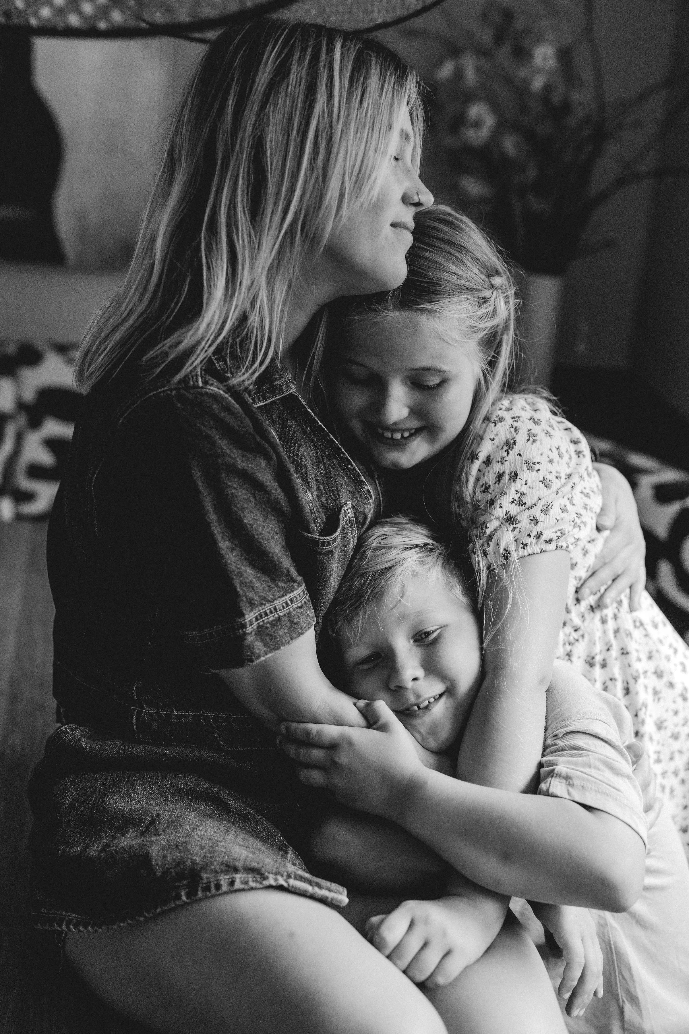 Een vrouw die omarmen wordt door twee kinderen, allemaal lachend en knuffelend.