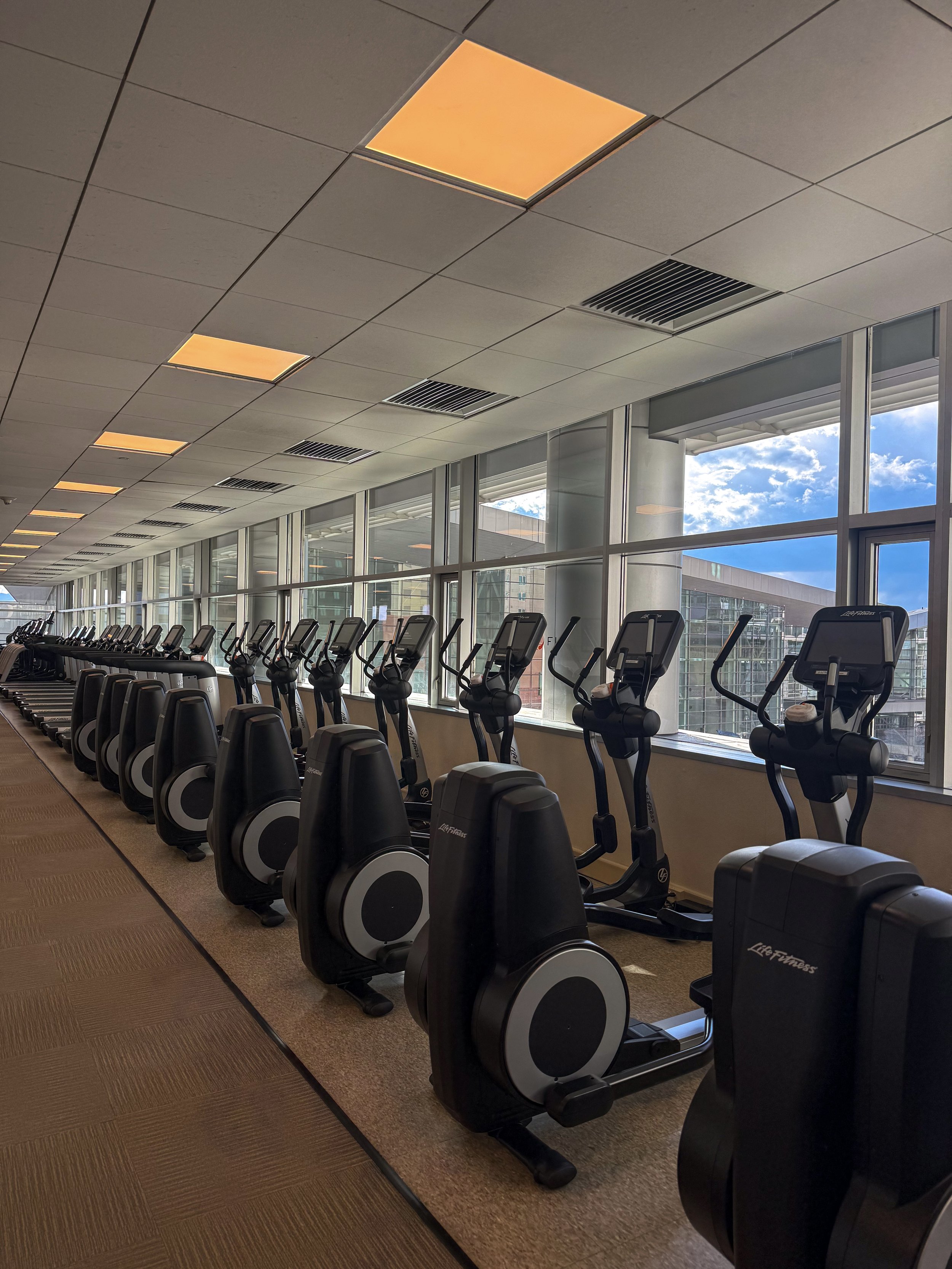 Spacious fitness center featuring rows of elliptical machines and treadmills overlooking downtown Denver