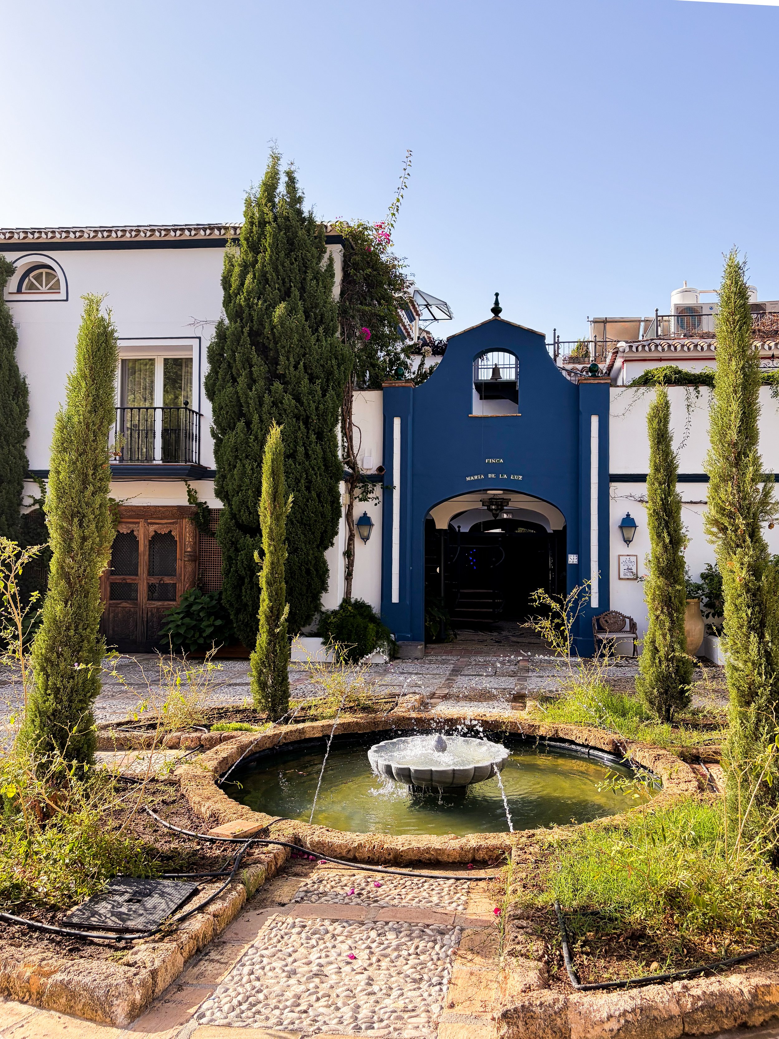 Traditional Andalusian courtyard with a fountain, cypress trees, and elegant entrance