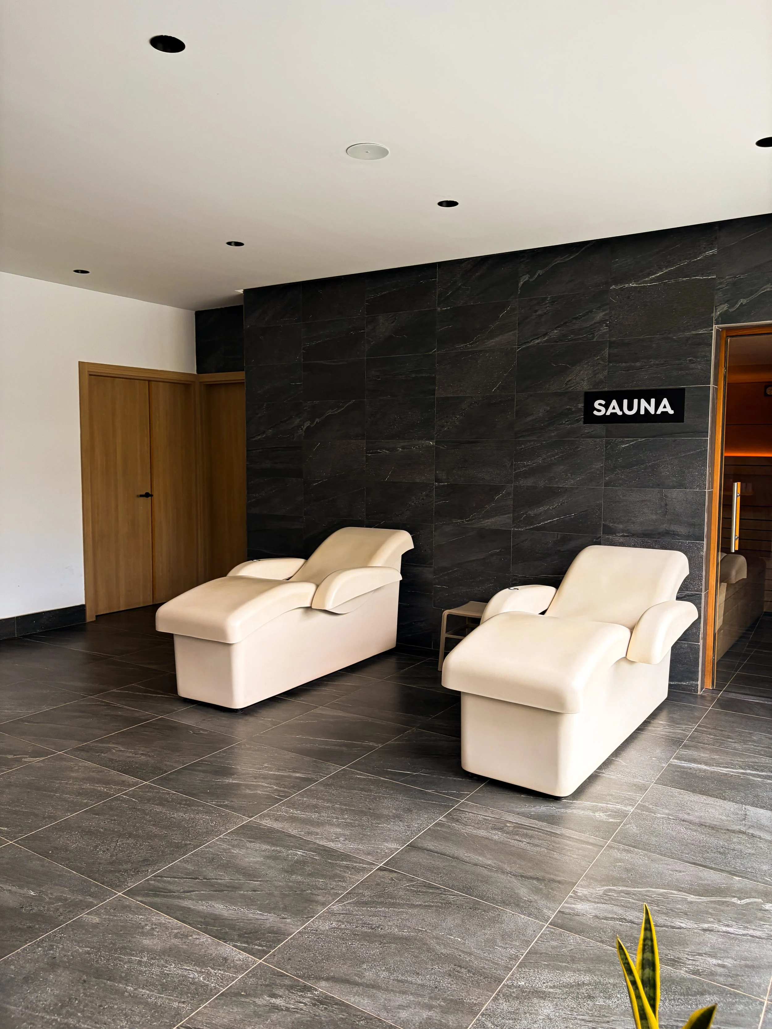 Peaceful spa relaxation area with two cushioned loungers, dark stone finishes, and access to the sauna