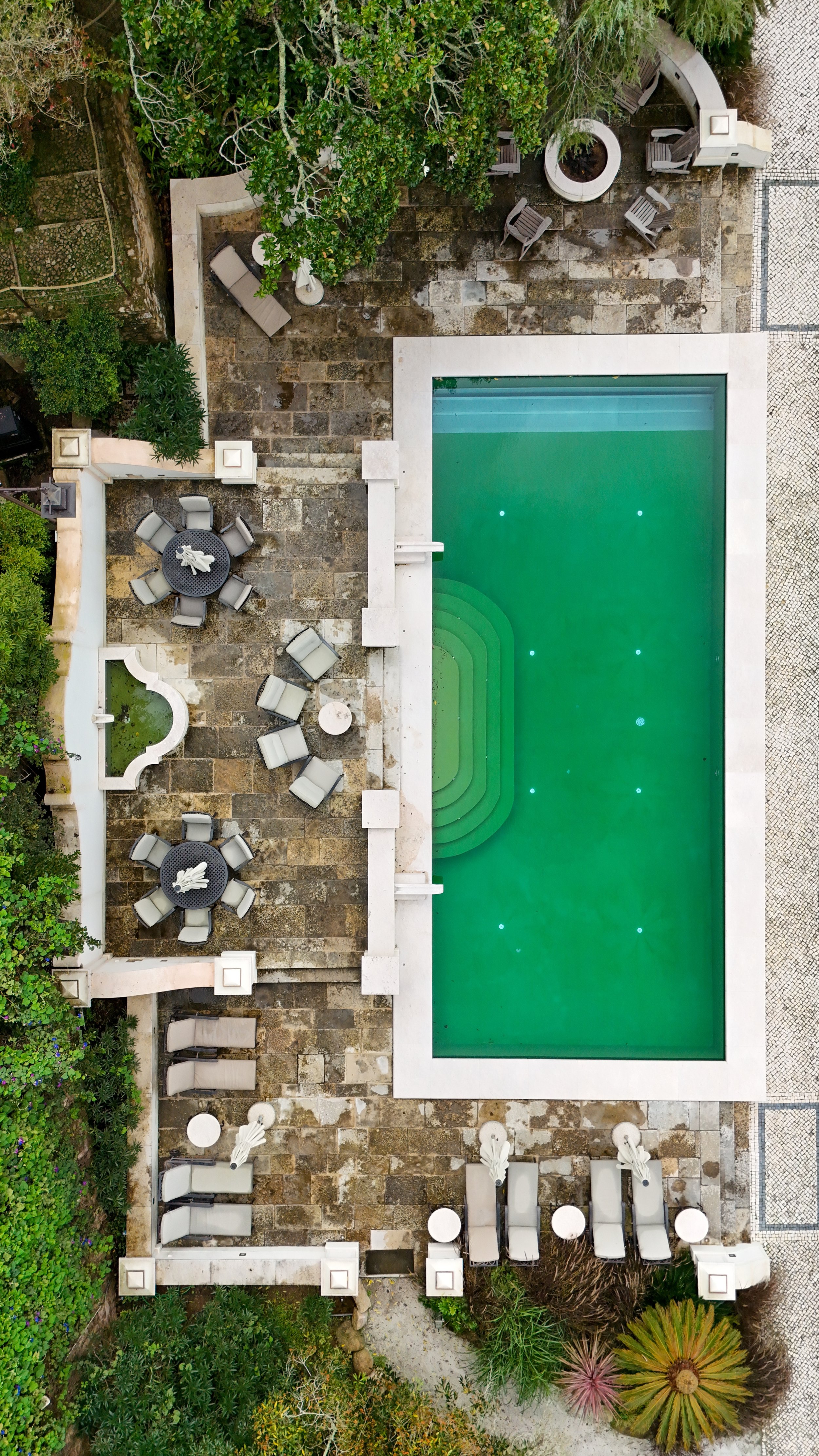 Aerial view of the swimming pool framed by stone terraces, loungers, and garden seating