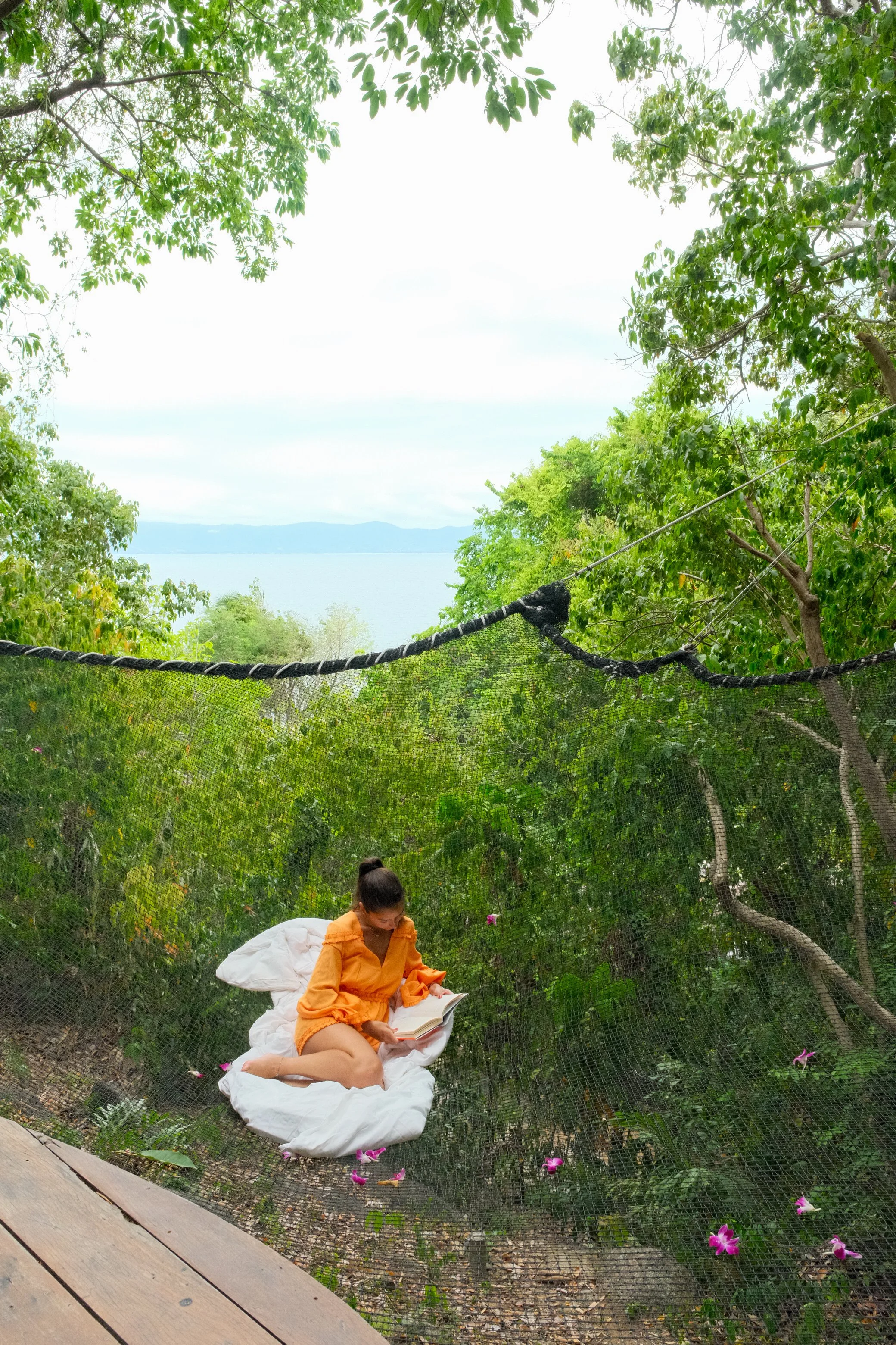 Guest reading on a suspended net above the tropical forest with distant sea views through the trees