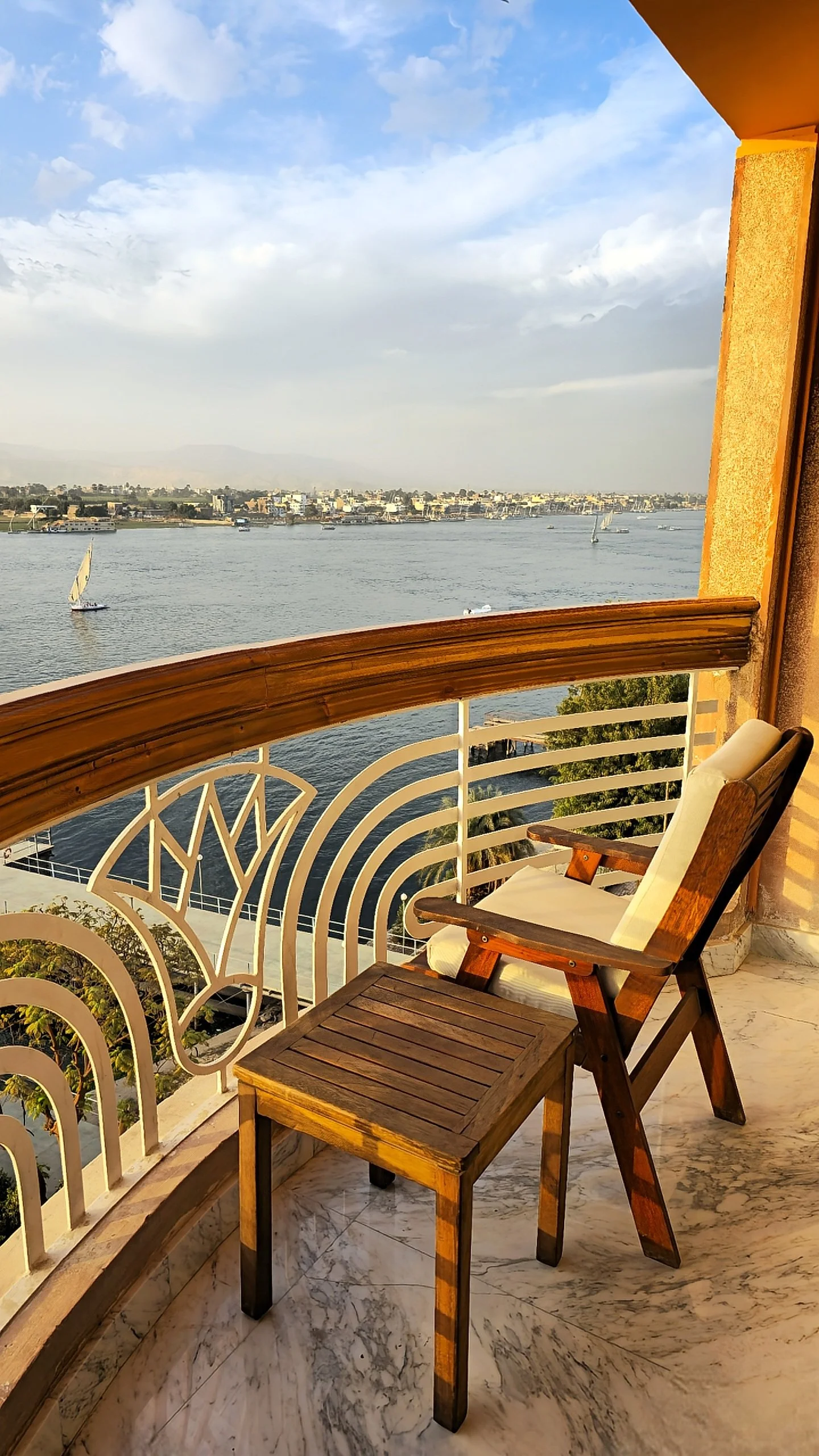 Private balcony with wooden chair and golden sunset views across the Nile and Luxor skyline, Sonesta St. George Hotel Luxor.