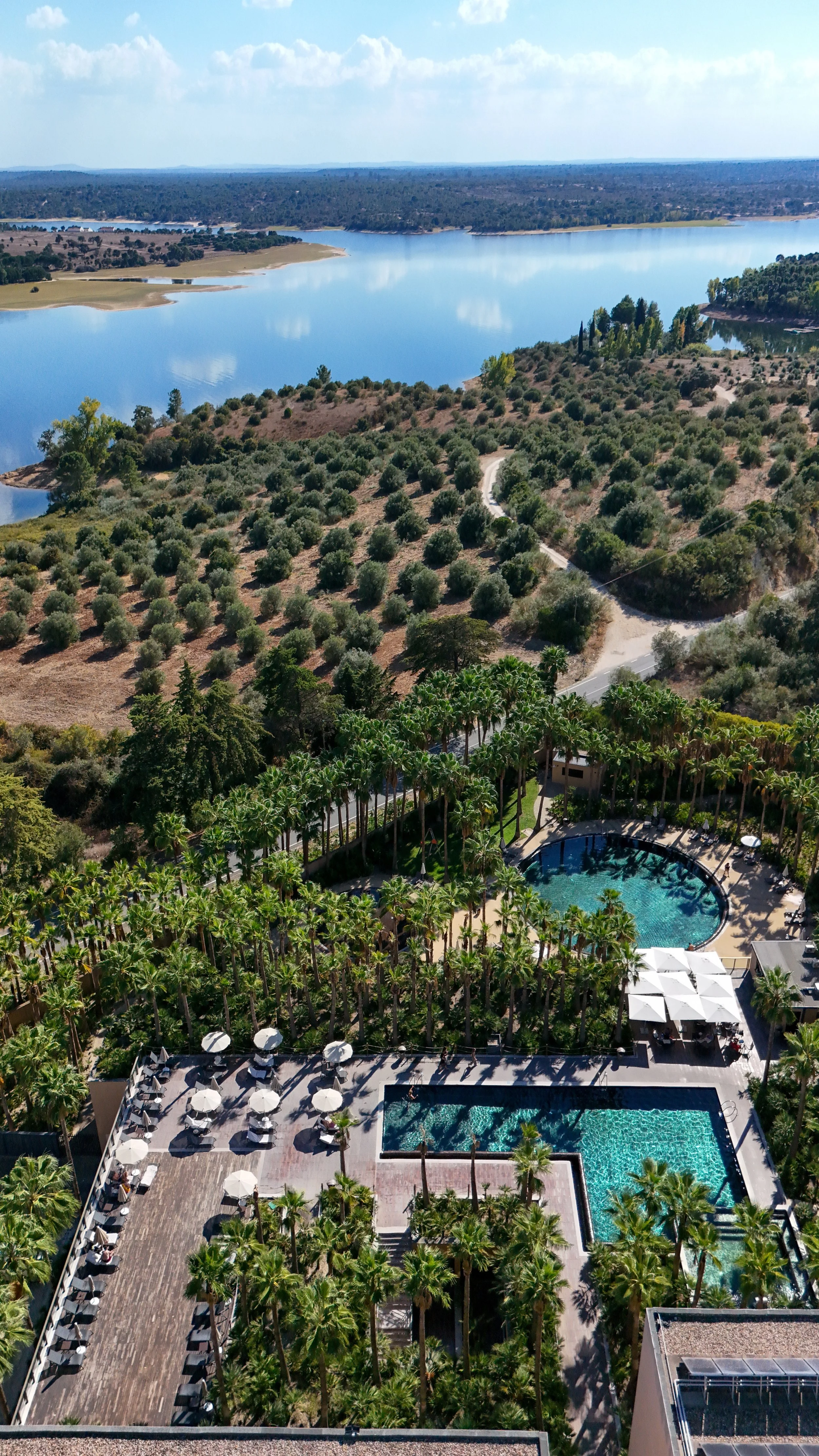 Aerial view of palm-lined resort swimming pools overlooking the Montargil reservoir and surrounding countryside