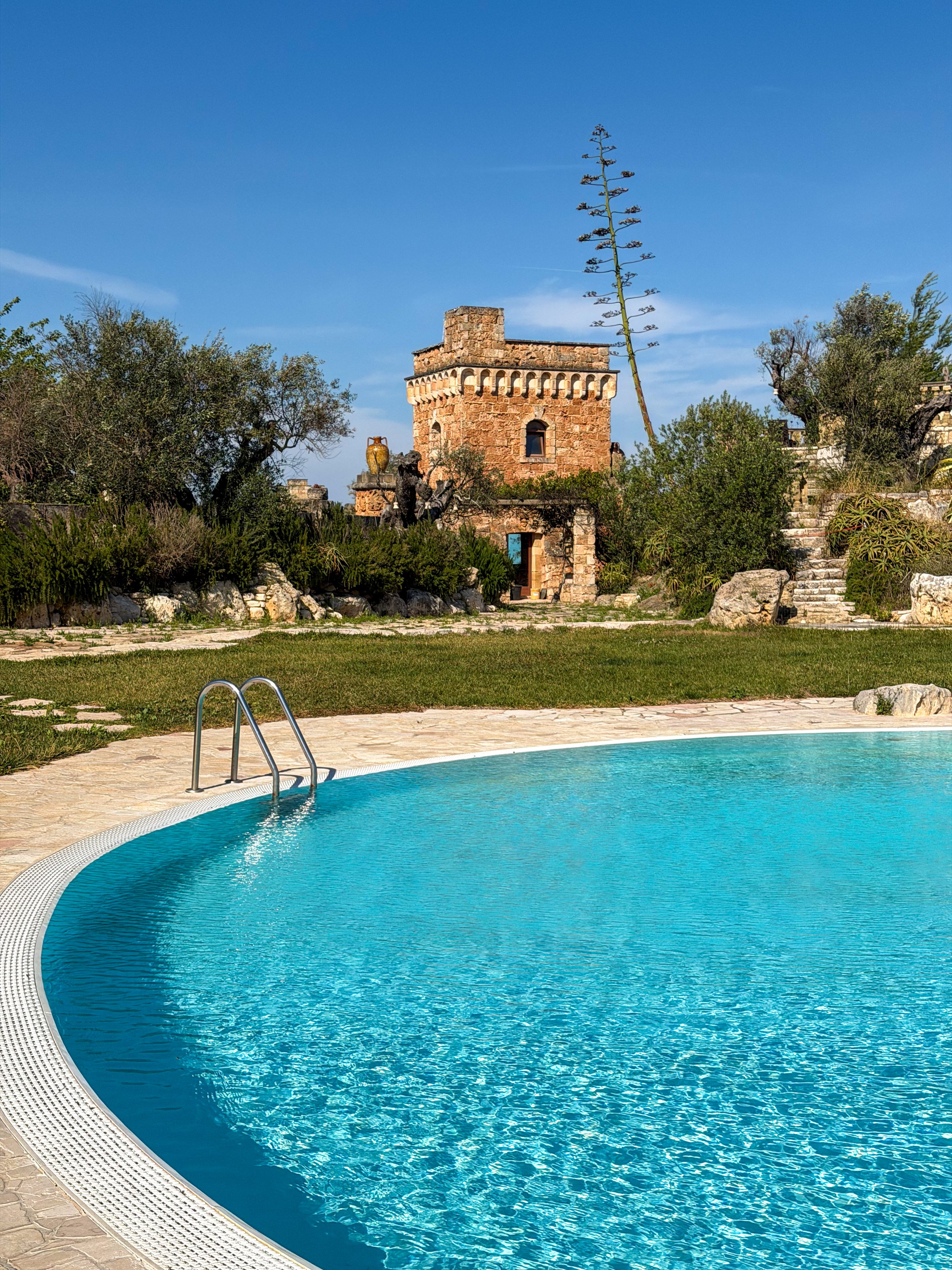 Outdoor swimming pool surrounded by historic stone architecture and Mediterranean gardens at Tenute Al Bano