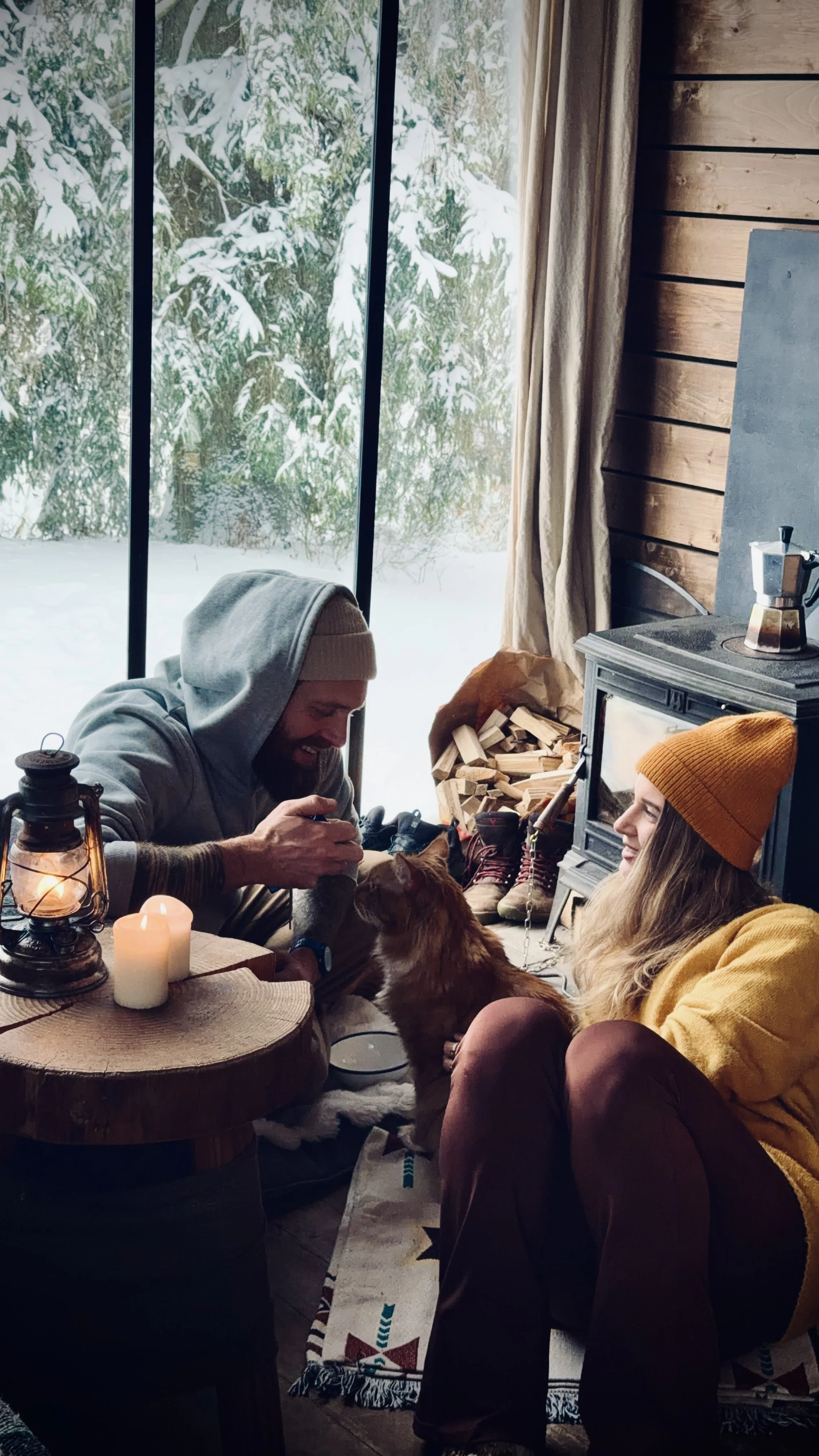 Couple relaxing beside the fireplace with the resident cabin cat during a snowy escape