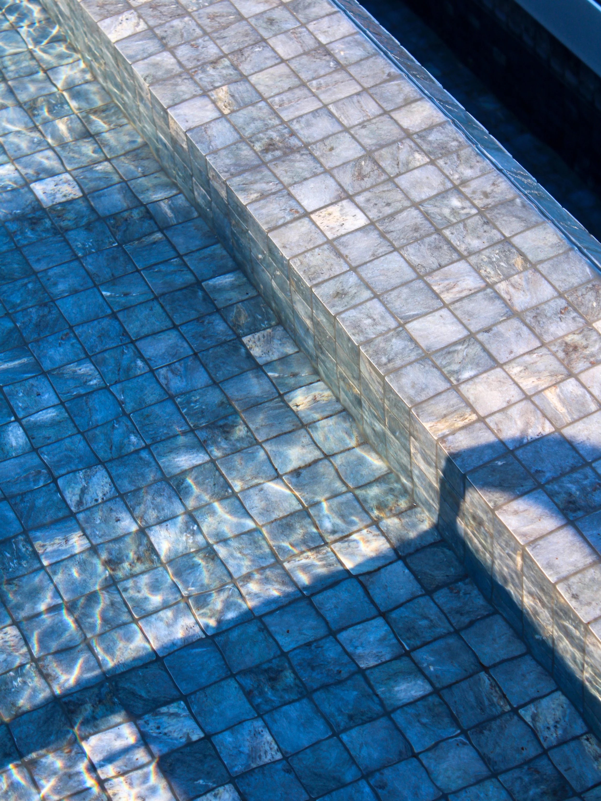 Close-up of shimmering pool tiles reflecting sunlight across crystal-clear water
