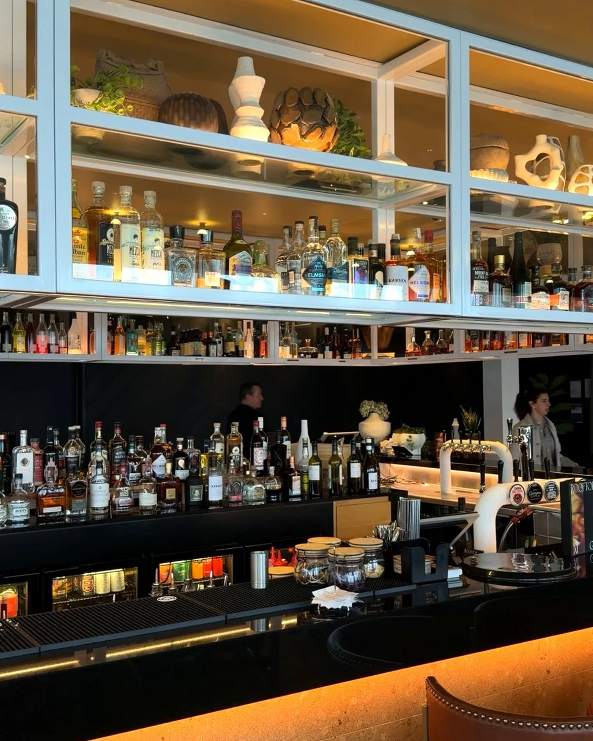 Stylish hotel bar featuring an extensive spirits collection, illuminated shelves, and contemporary decorative accents