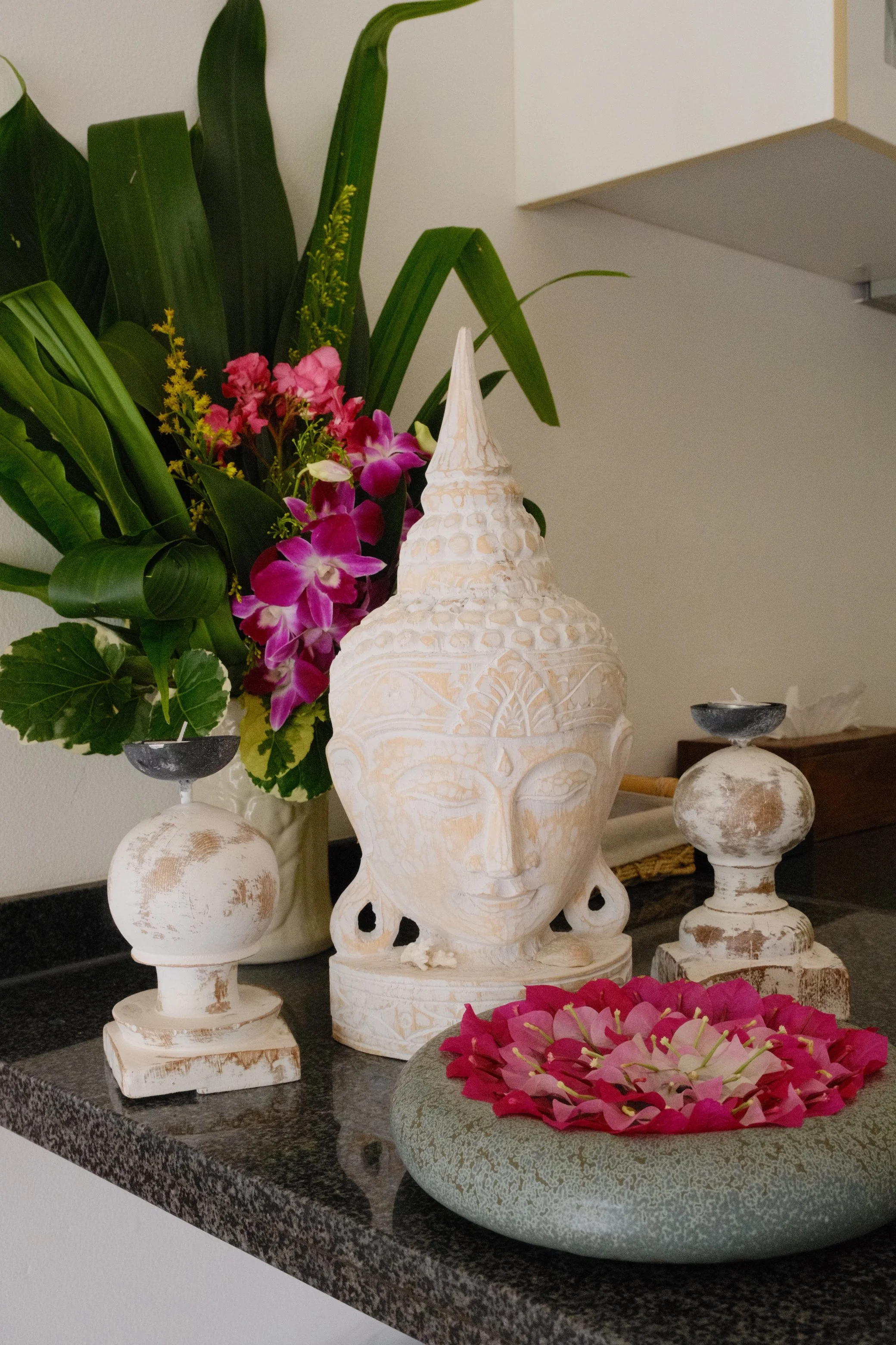 Thai-inspired Buddha sculpture surrounded by tropical flowers, candles, and decorative details