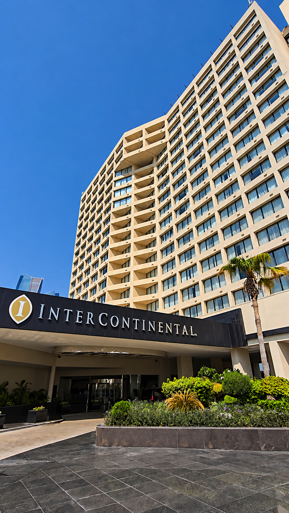 Modern luxury hotel exterior featuring a towering facade, grand entrance, landscaped gardens, and clear blue skies